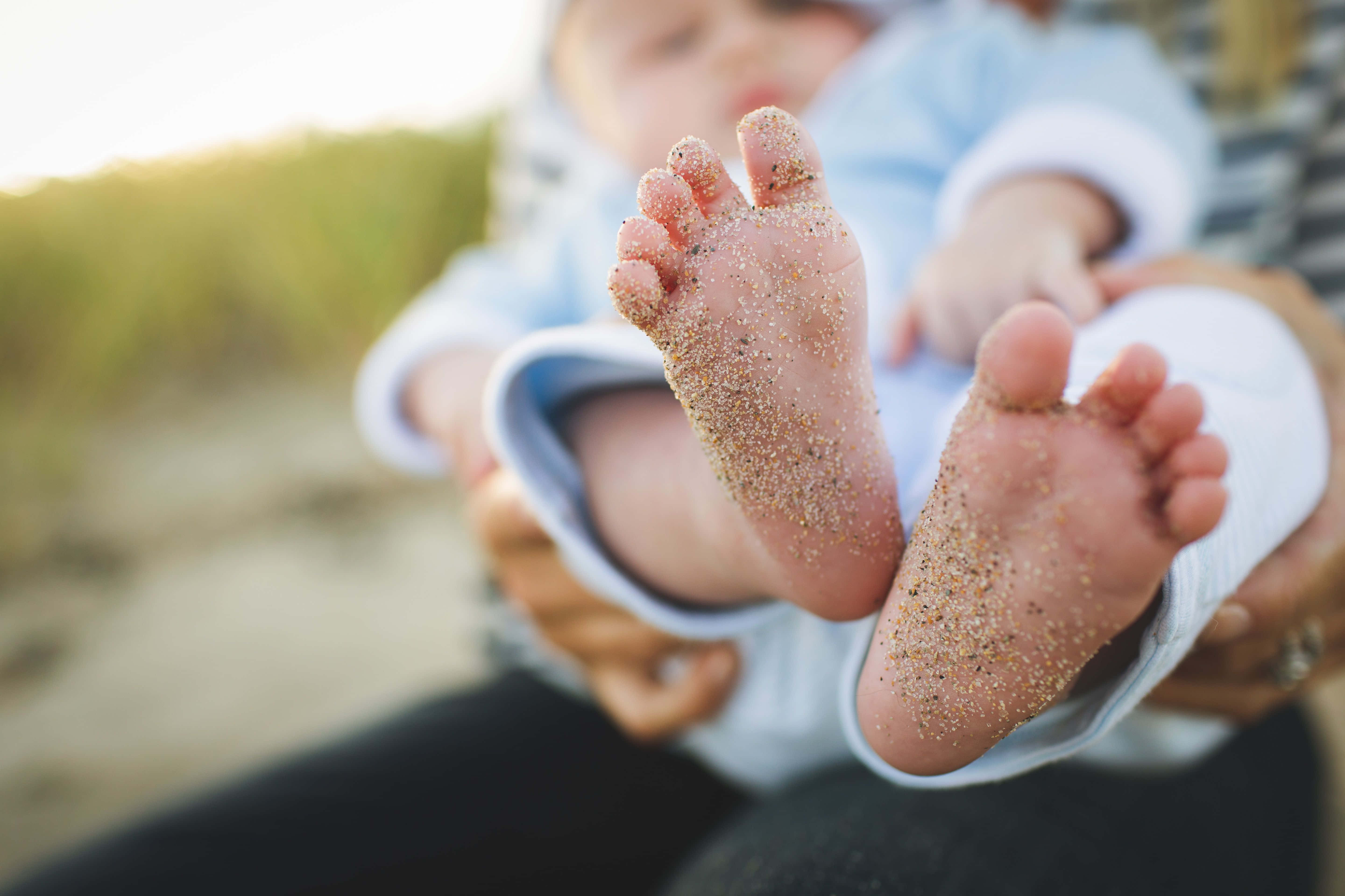 feet 桌布 壁紙 — 黃金時刻海灘上，成人輕柔地抱著嬰兒沾滿沙子的腳的近距離特寫。