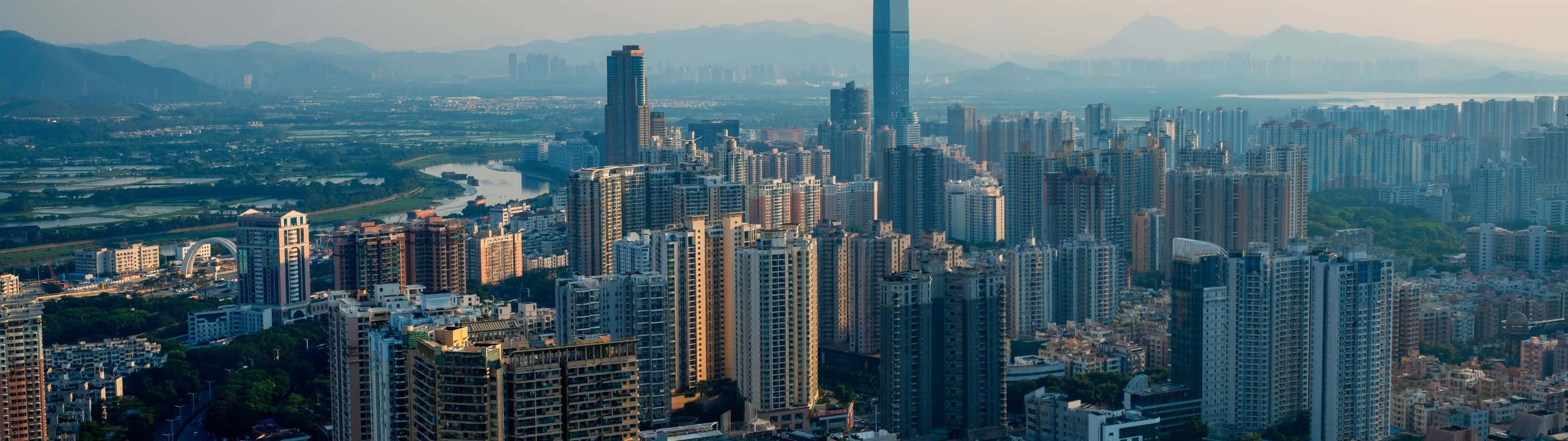 2732x768 桌布 壁紙 — 黃金時刻的廣闊城市天際線，高聳的摩天大樓和遠處的山脈在柔和朦朧的天空下。