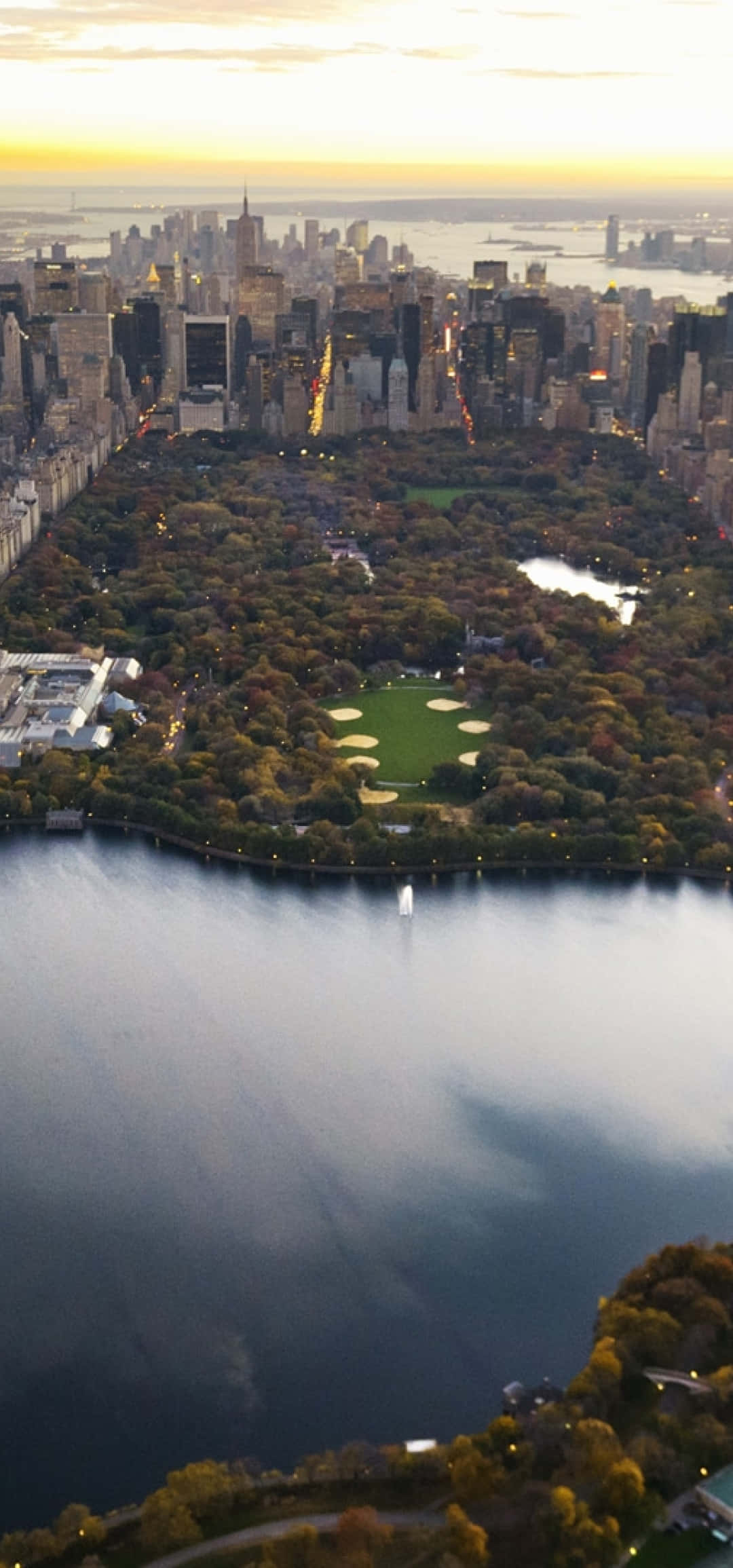 Panorama 桌布 壁紙 — 黃金時段中央公園的鳥瞰圖，秋天的樹木和城市天際線倒映在水中。