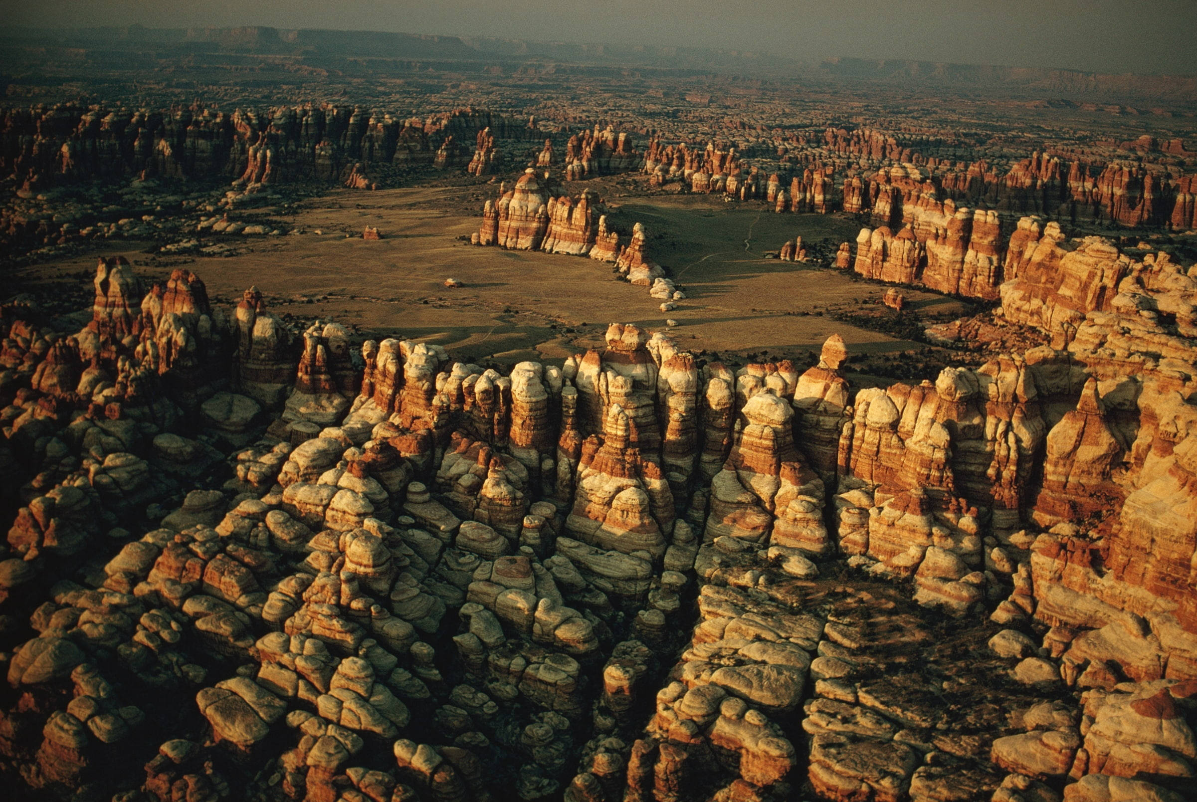 Canyonlands National Park 桌布 壁紙 — 黃金時段俯瞰廣闊沙漠峽谷中高聳的紅色和白色岩層的航拍圖。