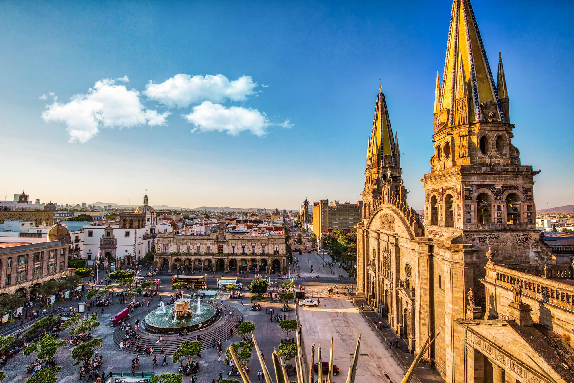 Guadalajara 桌布 壁紙 — 黃金時段充滿活力的城市廣場，宏偉的大教堂和熙熙攘攘的噴泉在清澈的藍天下。