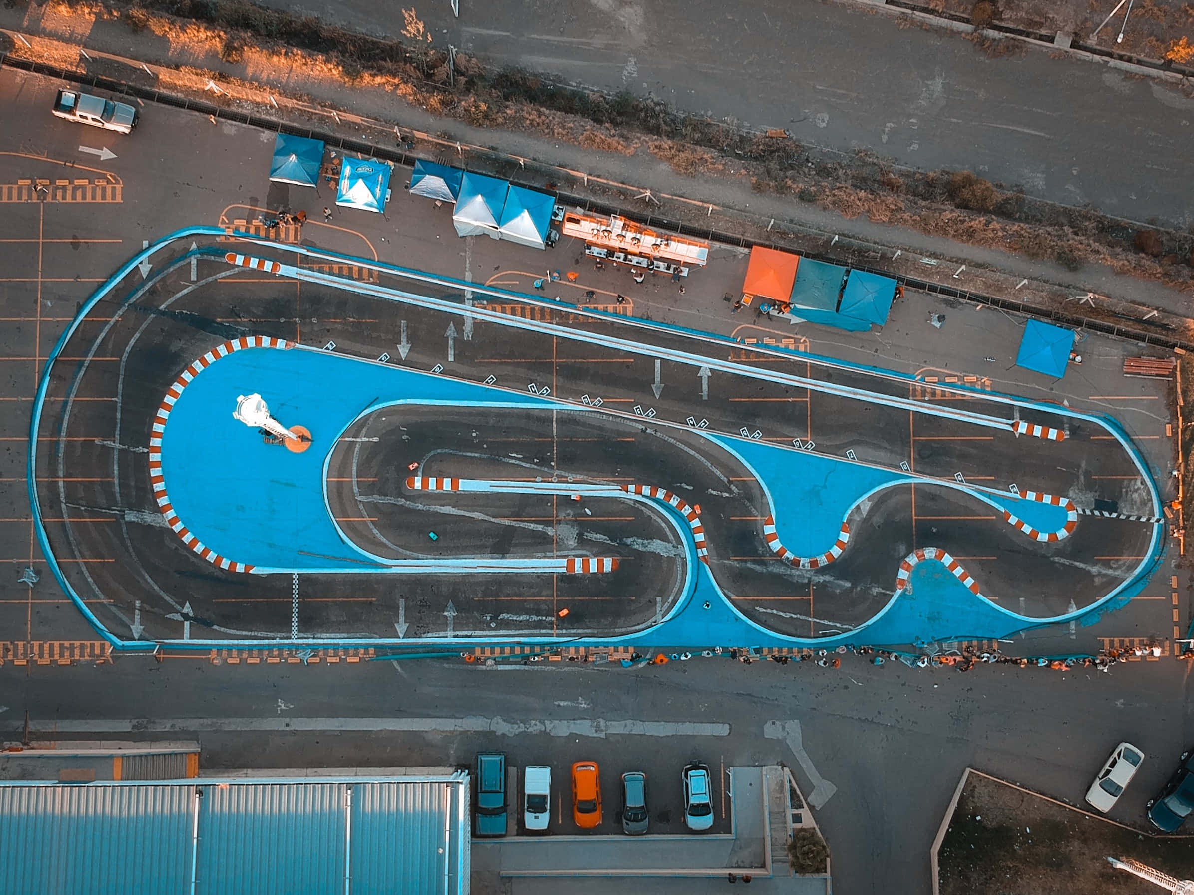 Race Track 桌布 壁紙 — 黃金時段城市停車場中蜿蜒的鮮藍色高卡車賽道鳥瞰圖。