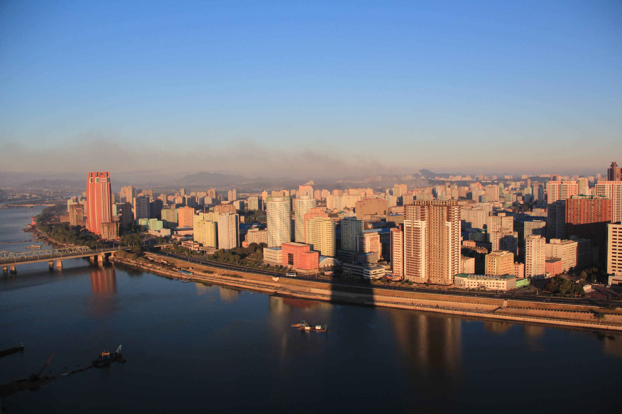 韓國 桌布 壁紙 — 黃金時段沿寬闊河流延伸的廣闊城市景觀鳥瞰圖，帶有長長的陰影和寧靜的水面倒影。