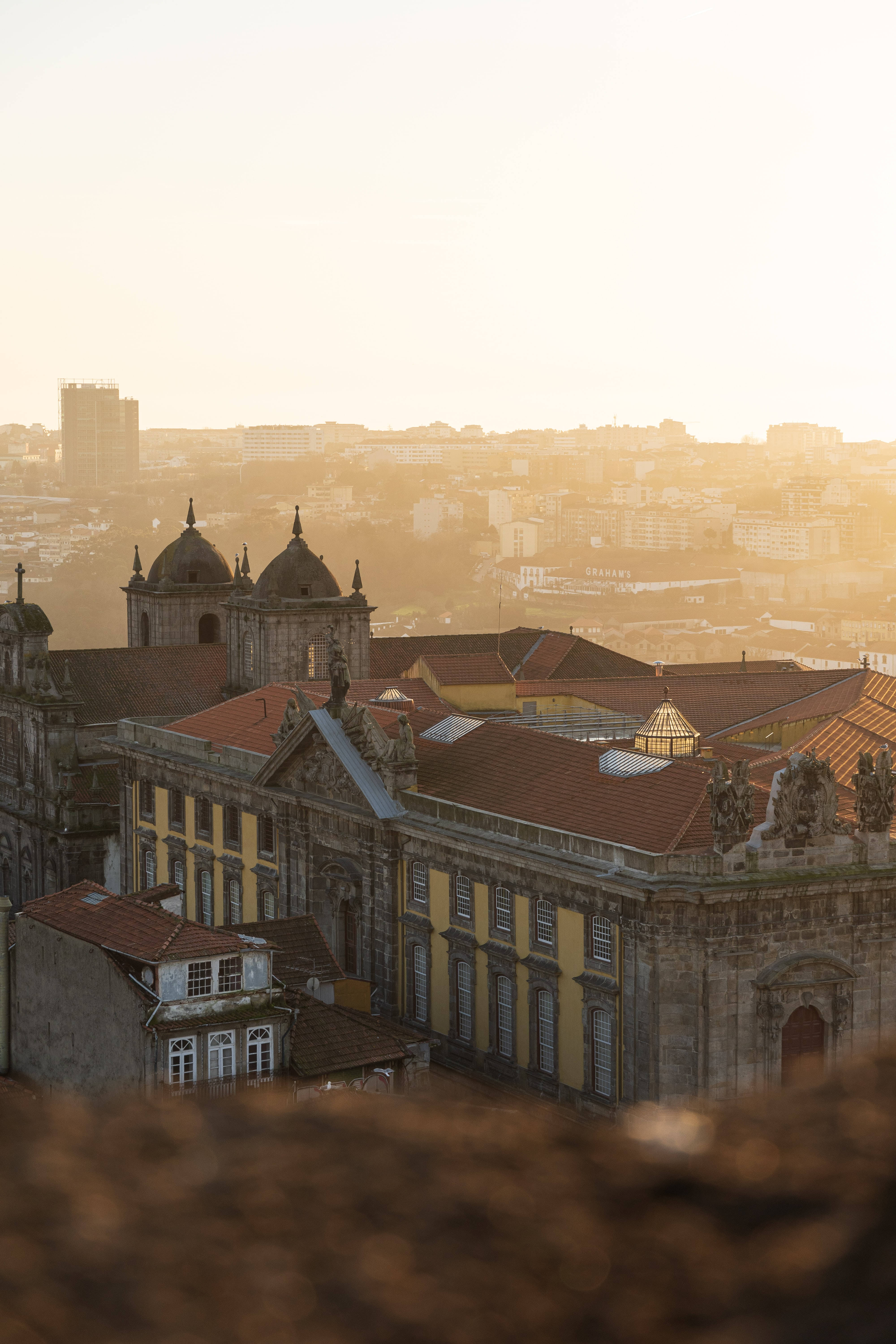 Portugal 桌布 壁紙 — 黃金時段的陽光以溫暖的琥珀色調沐浴在歷史悠久的歐洲屋頂和圓頂教堂上，籠罩在朦朧的城市景觀中。