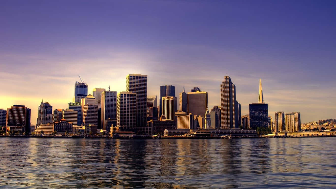 1366x768 San Francisco 桌布 壁紙 — 黃金時段的陽光以溫暖色調沐浴舊金山天際線，摩天大樓倒映在平靜的海灣水面上。