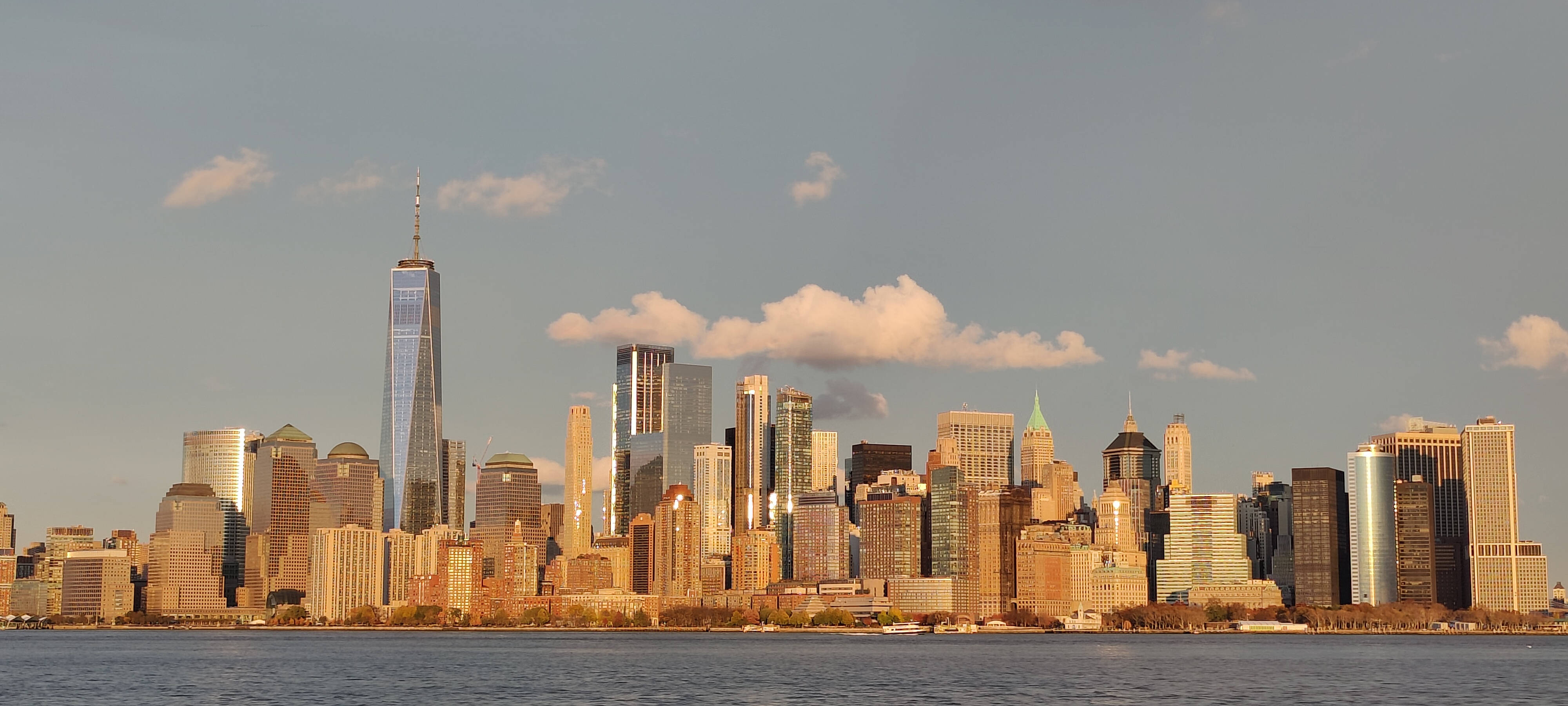 Nyc Aesthetic 桌布 壁紙 — 黃金時段的陽光以溫暖色調沐浴著標誌性的紐約市天際線，摩天大樓在下方平靜的水面上倒映。