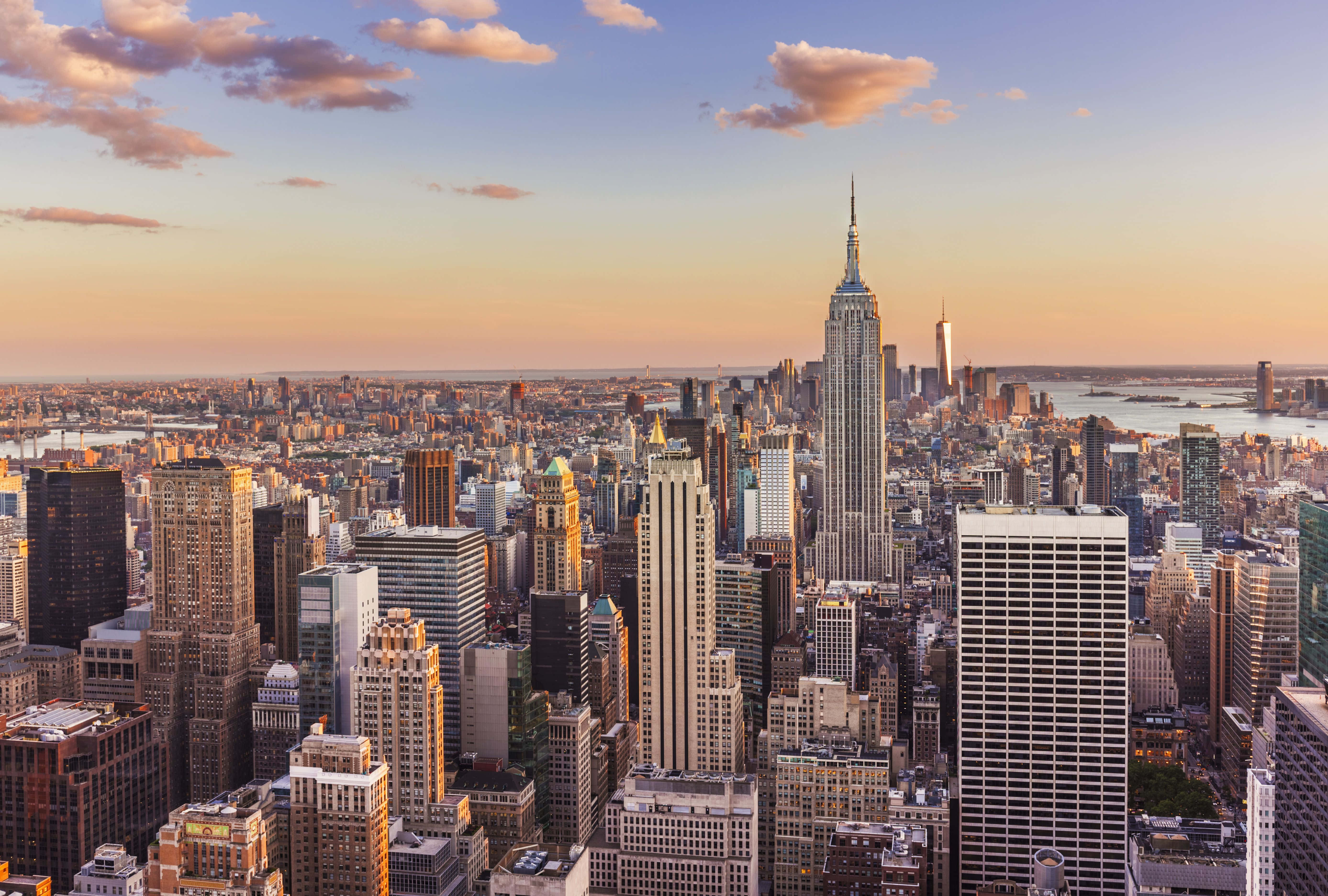 New York 桌布 壁紙 — 黃金時段的陽光以溫暖色調沐浴著紐約市高聳的摩天大樓，雲朵在城市天際線上方飄移。