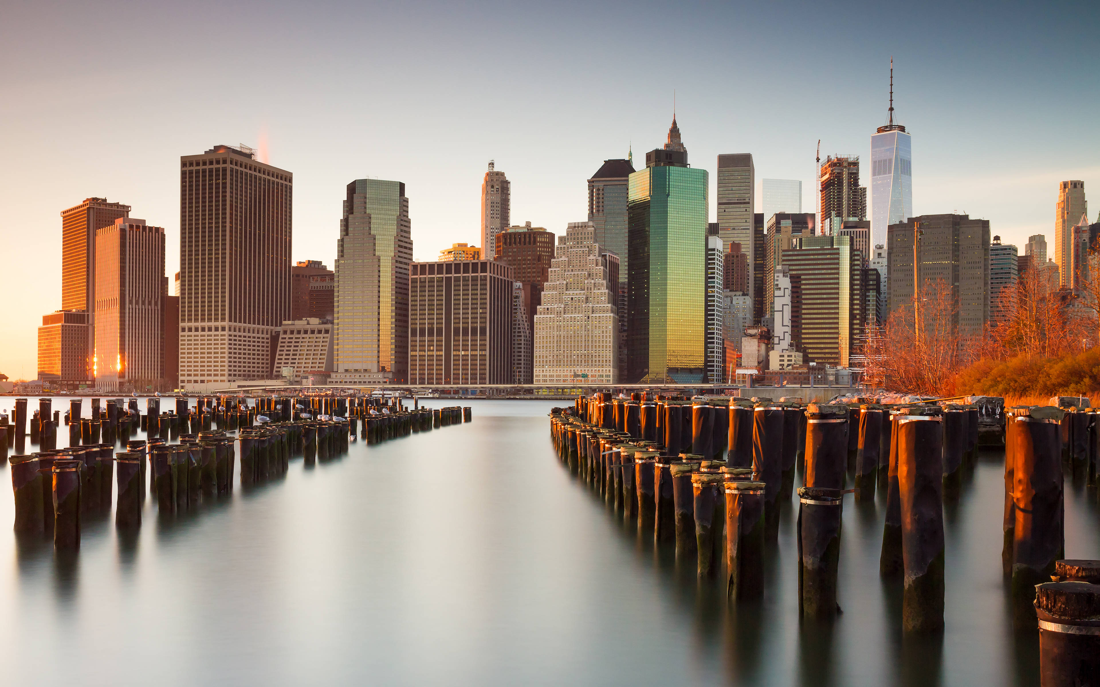 New York Skyline 桌布 壁紙 — 黃金時段的陽光沐浴著紐約市的天際線，平靜的水面映照出摩天大樓和歷經風霜的碼頭。