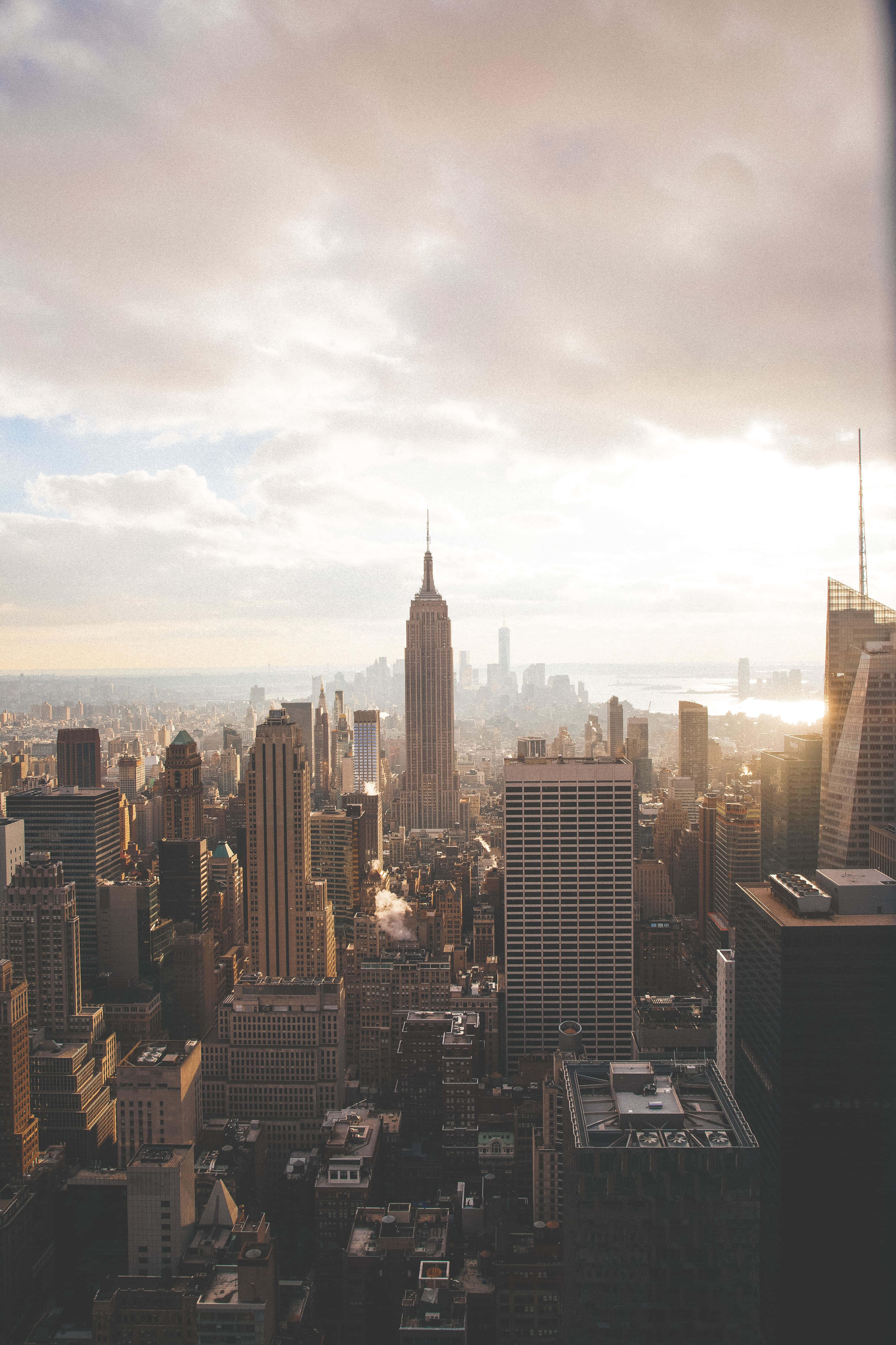 Empire State Building 桌布 壁紙 — 黃金時段紐約市天際線的空中景觀，帝國大廈在柔和的雲層下聳立於密集的城市建築之上。