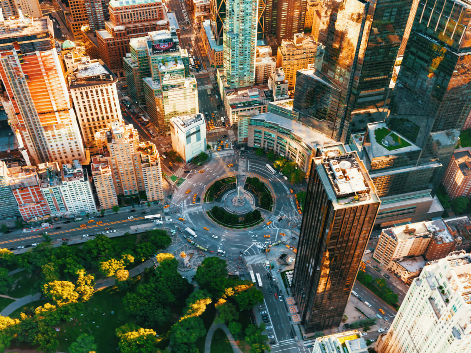 New York City 4K Ultra HD 桌布 壁紙 — 黃金時段繁忙城市景觀的鳥瞰圖，高聳的摩天大樓環繞著圓形交通迴旋處和下方鬱鬱蔥蔥的綠色公園。