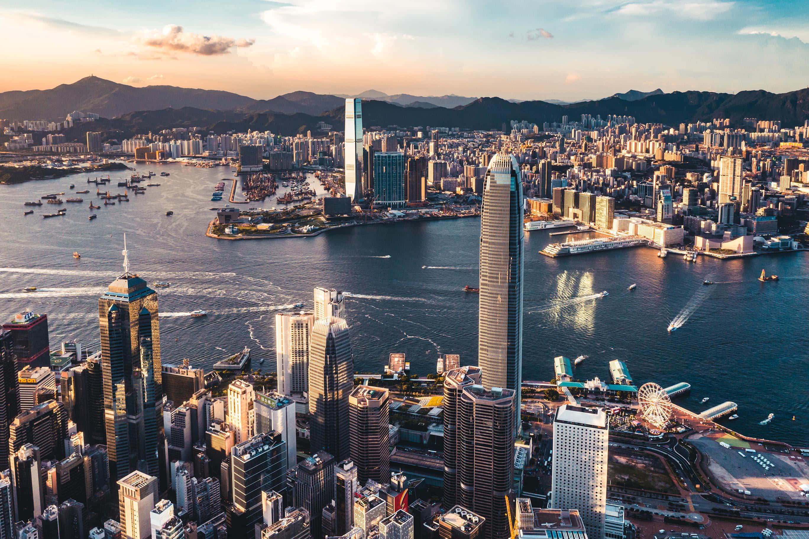 香港 桌布 壁紙 — 黃金時段香港天際線的鳥瞰圖，摩天大樓將溫暖的光線反射到充滿船隻的維多利亞港上。
