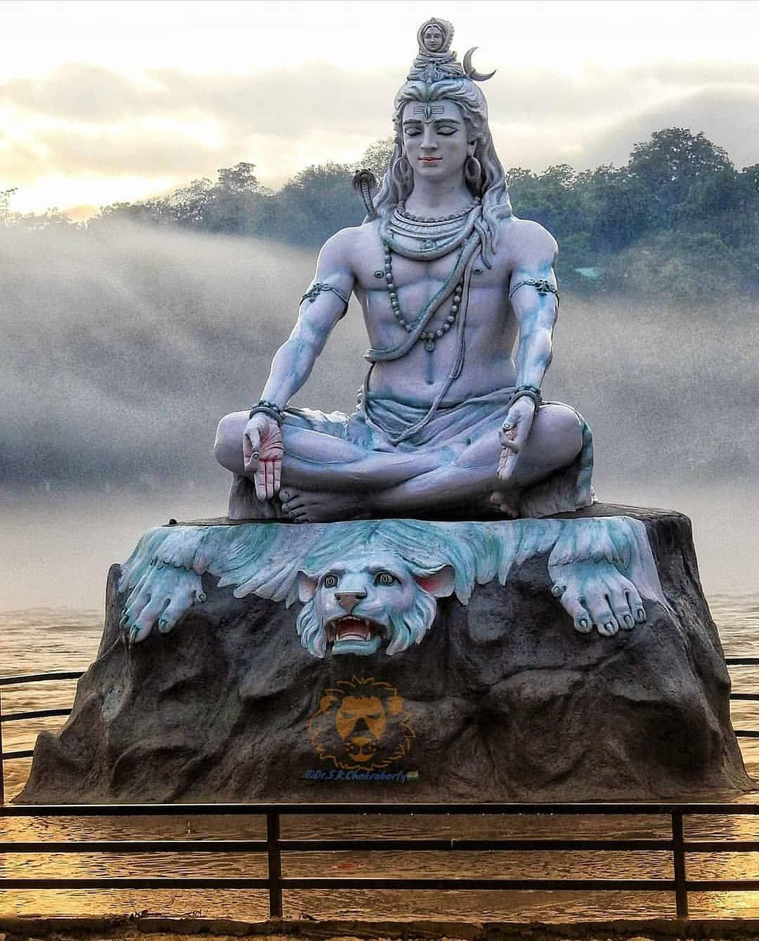 India 桌布 壁紙 — 黎明時分，一尊寧靜的藍色濕婆神像在霧氣瀰漫的河邊獅頭岩石上冥想。