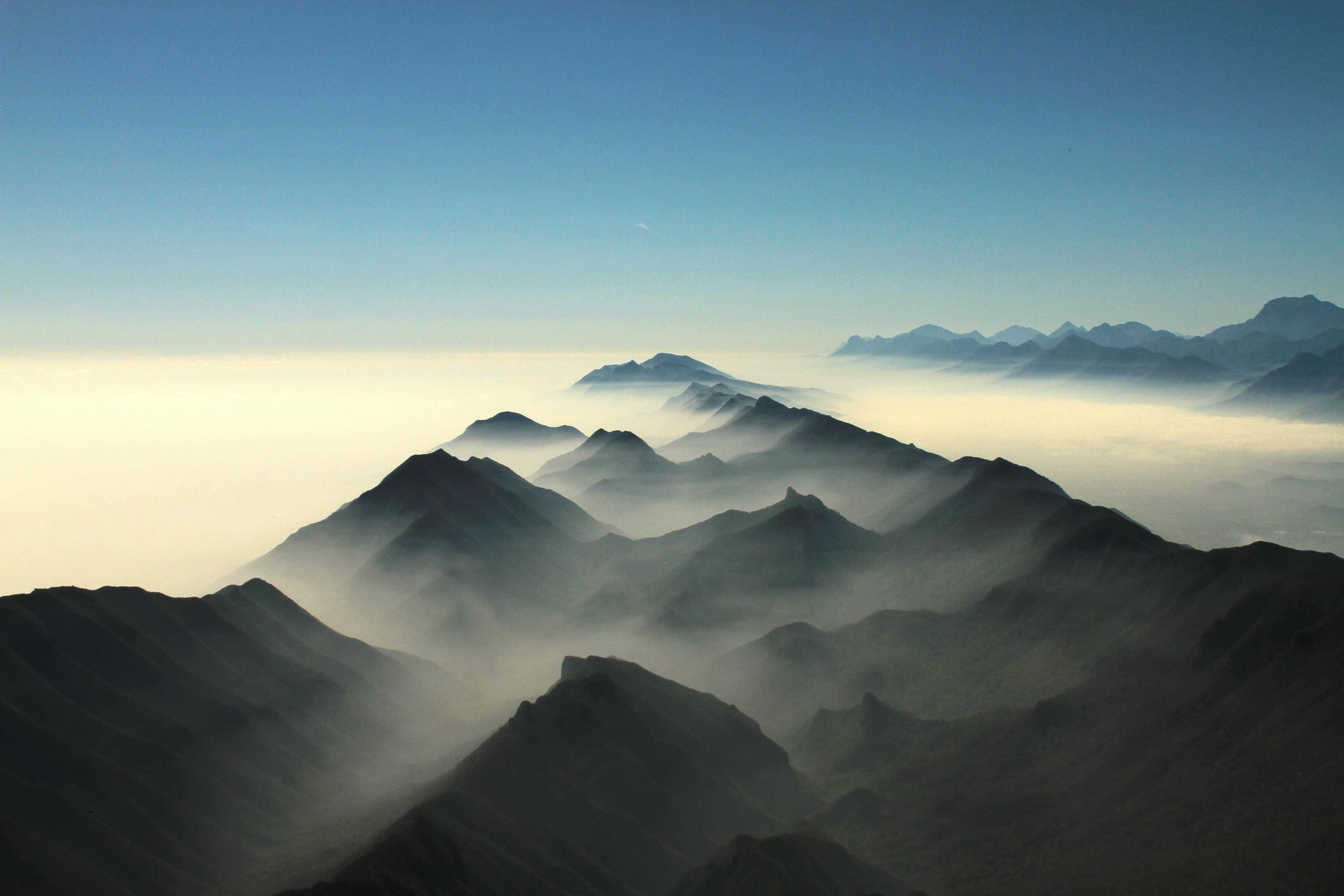 Soothing 桌布 壁紙 — 黎明時分，在清澈的藍天下，剪影般的山峰從霧海中升起。