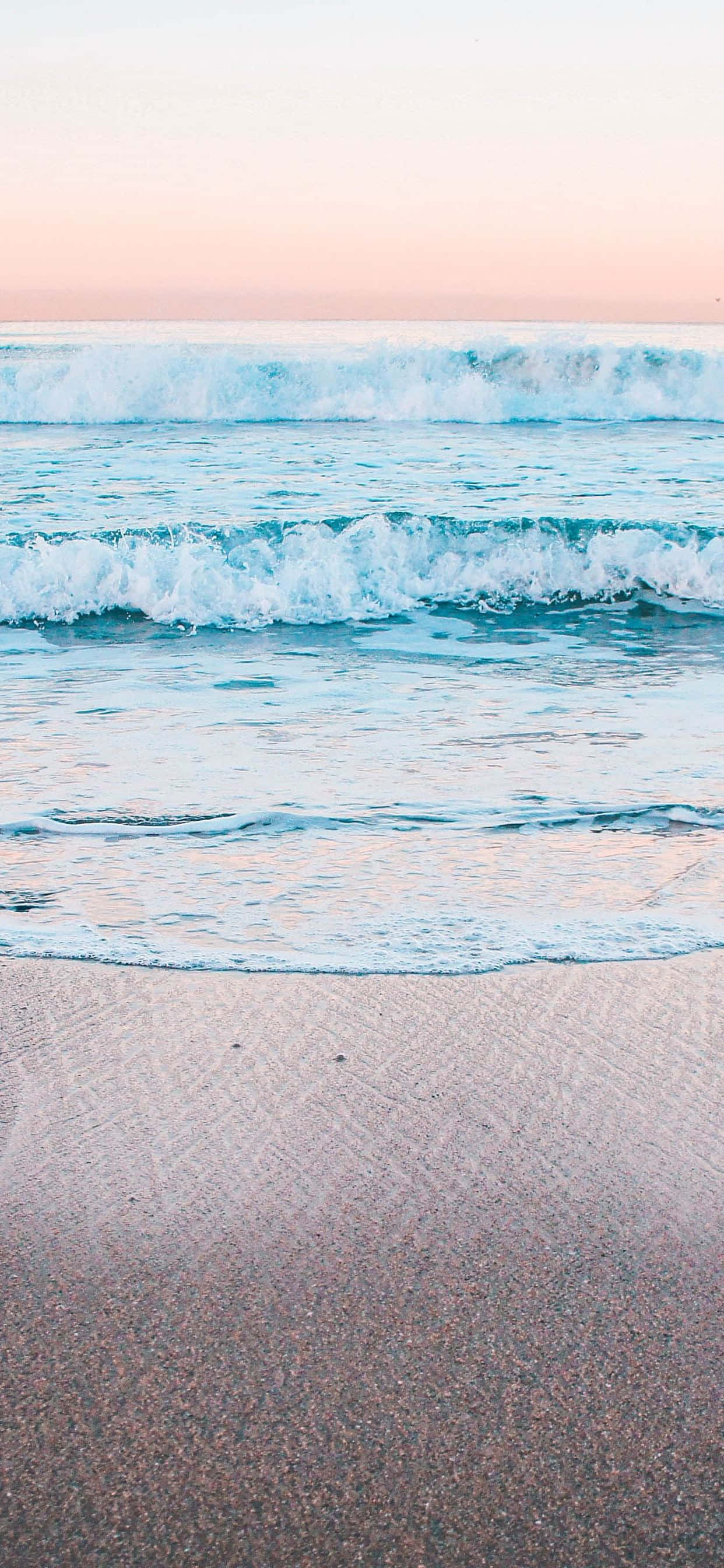Calming iPhone 桌布 壁紙 — 黎明時分，柔和的粉紅色和藍色波浪在質感沙灘上翻滾，天空呈現粉彩調。
