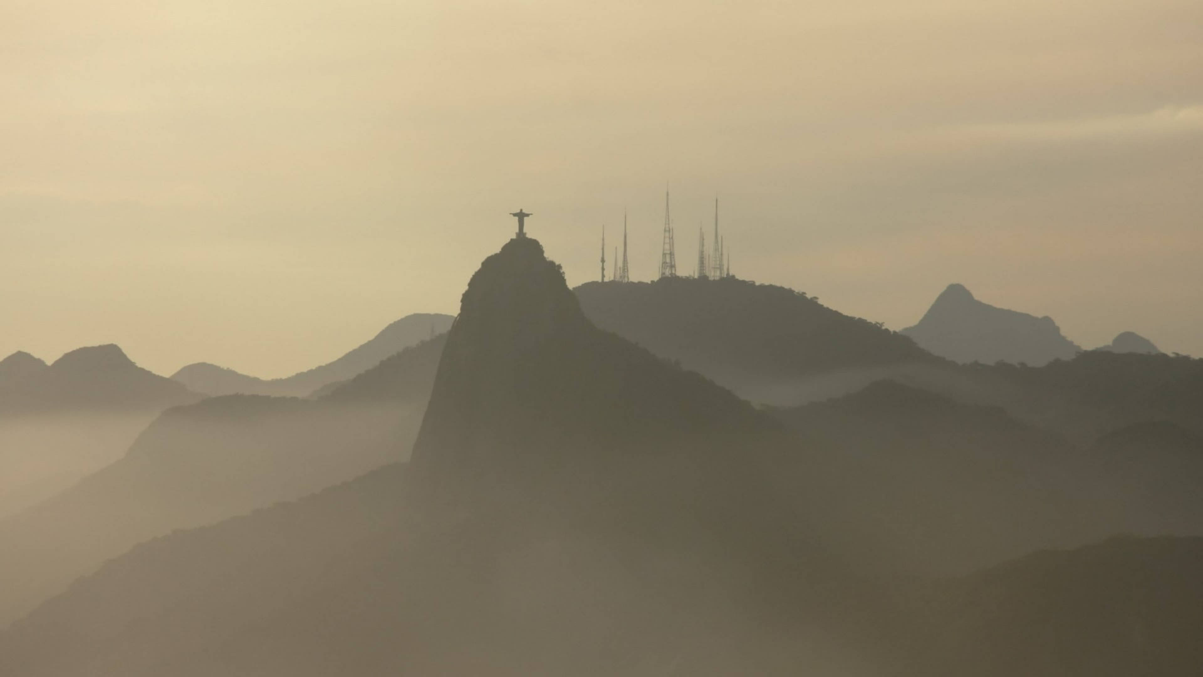 rio 桌布 壁紙 — 黎明時分，科爾科瓦多山頂上基督救世主雕像的剪影在雲霧繚繞的山峰上聳立。