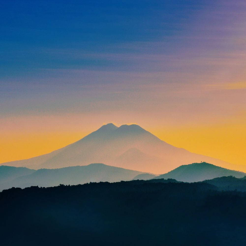 美學平板 桌布 壁紙 — 黎明時分，雄偉的山脈輪廓在深藍紫色和金色橙色的漸變天空中升起。