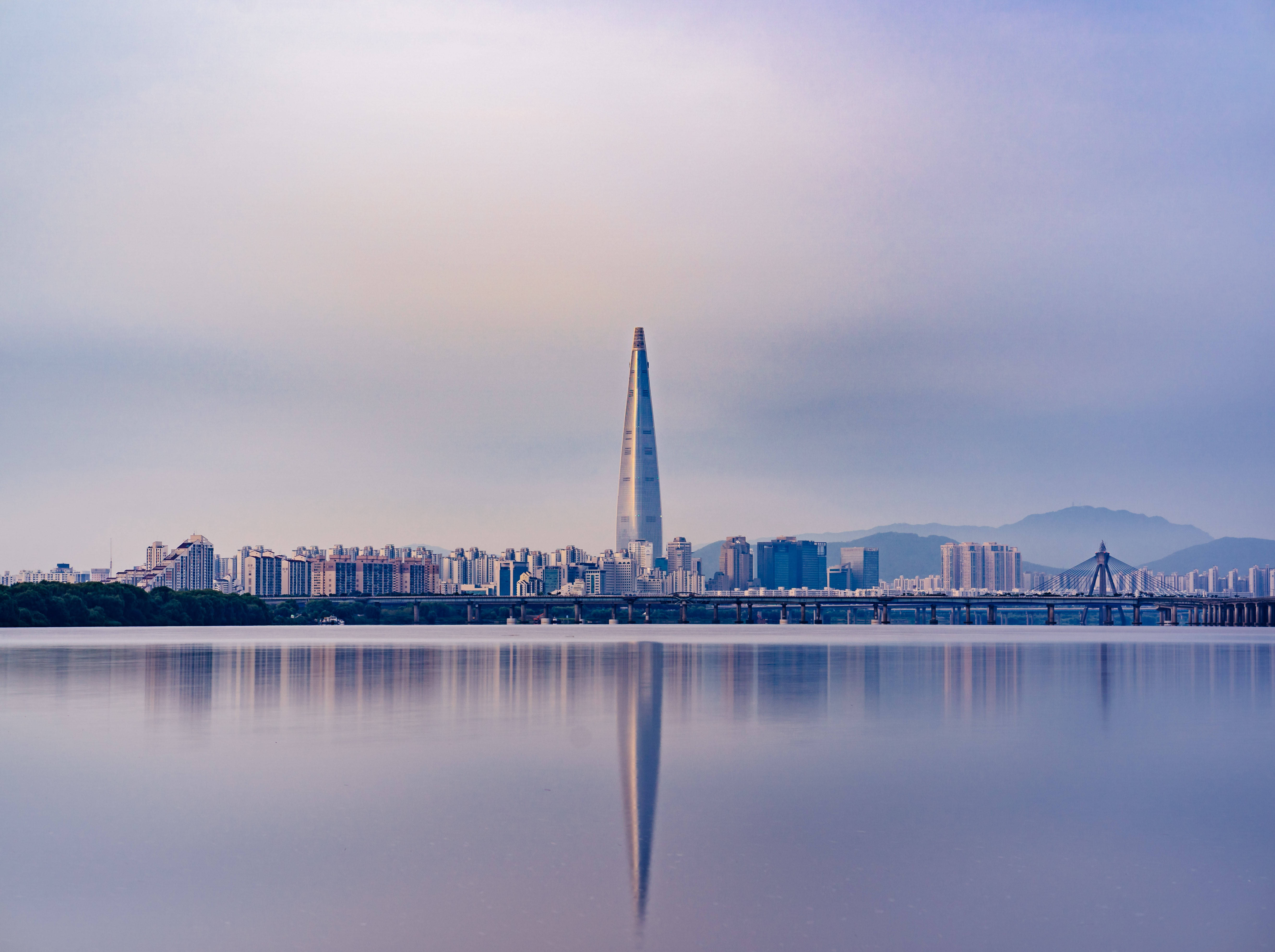 South Korea 桌布 壁紙 — 黎明時分寧靜的城市景觀，樂天世界塔在柔和粉彩天空下倒映在平靜的水面上。