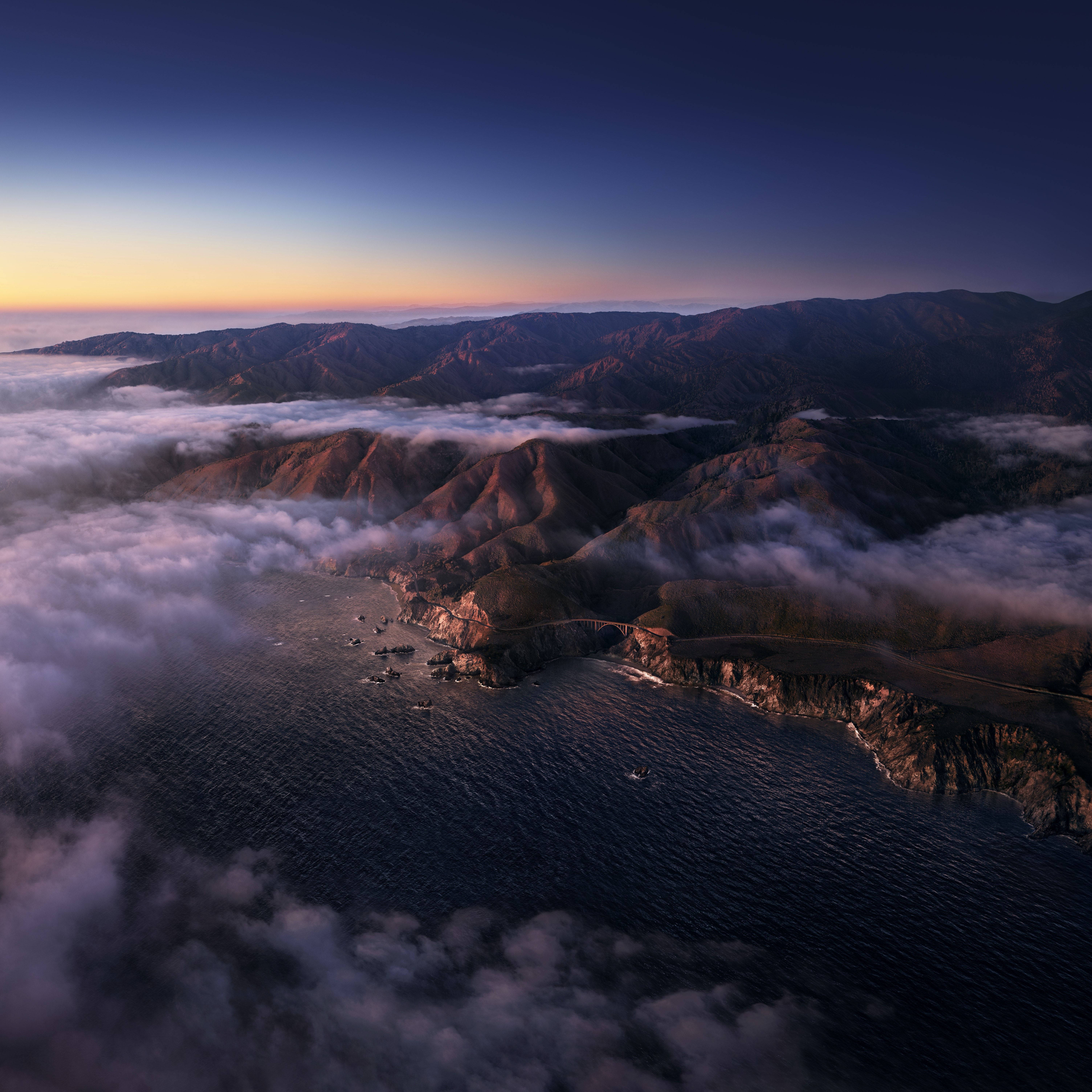 Cloud Aesthetic 桌布 壁紙 — 黎明時分海岸橋樑的鳥瞰圖，山脈在海霧之上升起，下方是深藍色的海洋。