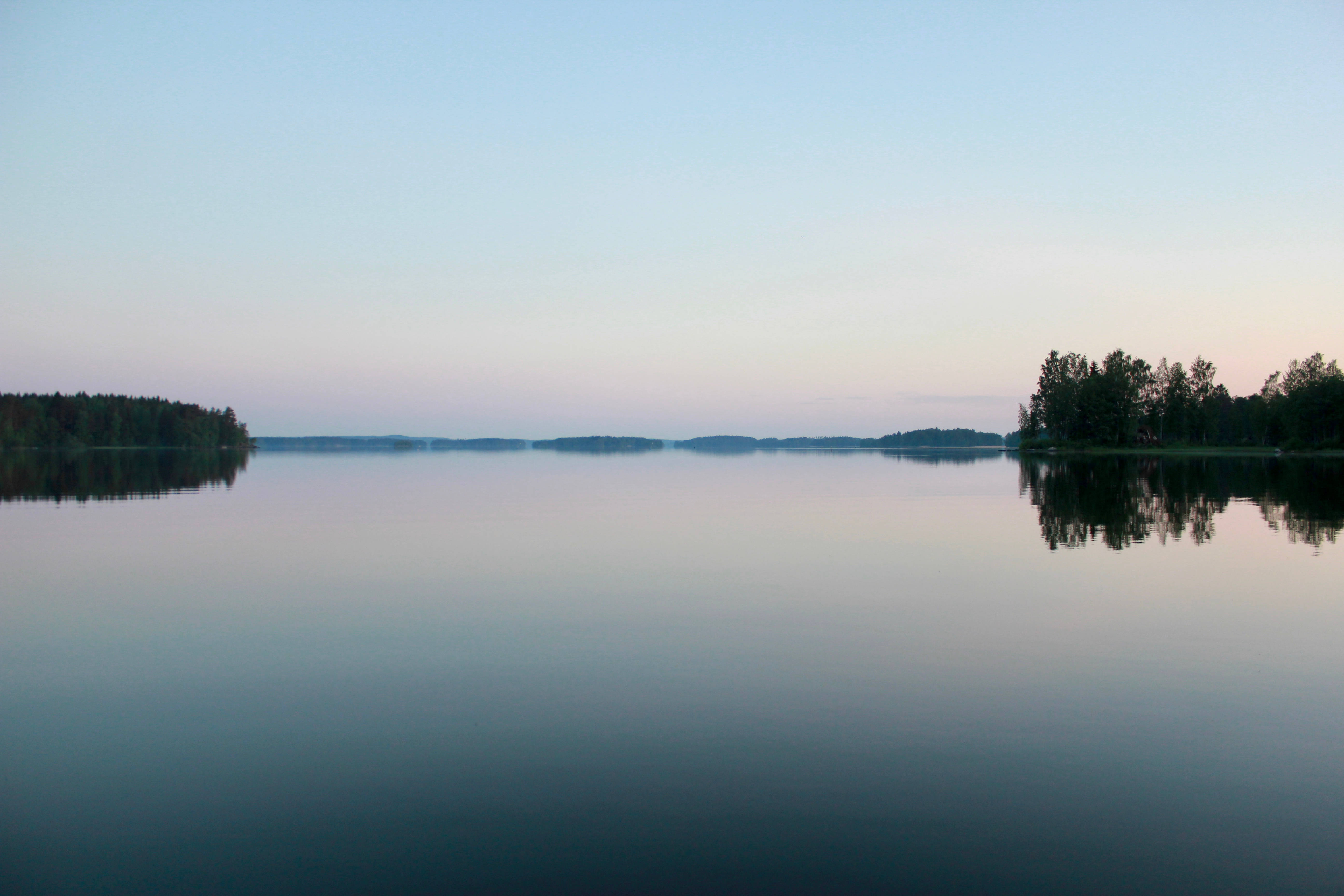 Finland 桌布 壁紙 — 黎明時分的寧靜湖泊，完美靜止地倒映著柔和粉彩的天空和遠處樹木成行的岸邊。