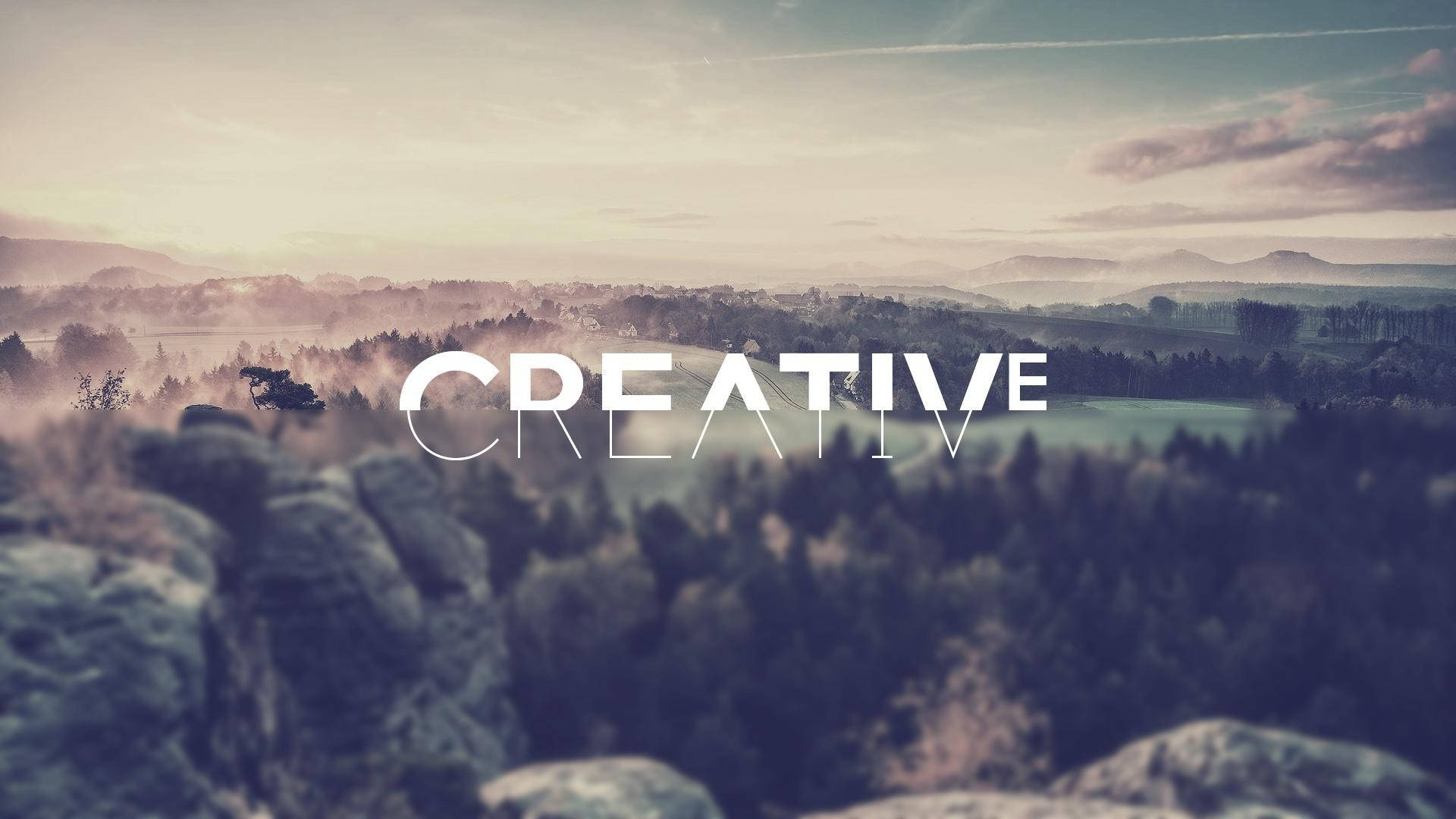 Typography 桌布 壁紙 — 黎明時分霧氣瀰漫的山景，岩石前景上覆蓋著粗體白色「CREATIVE」文字。