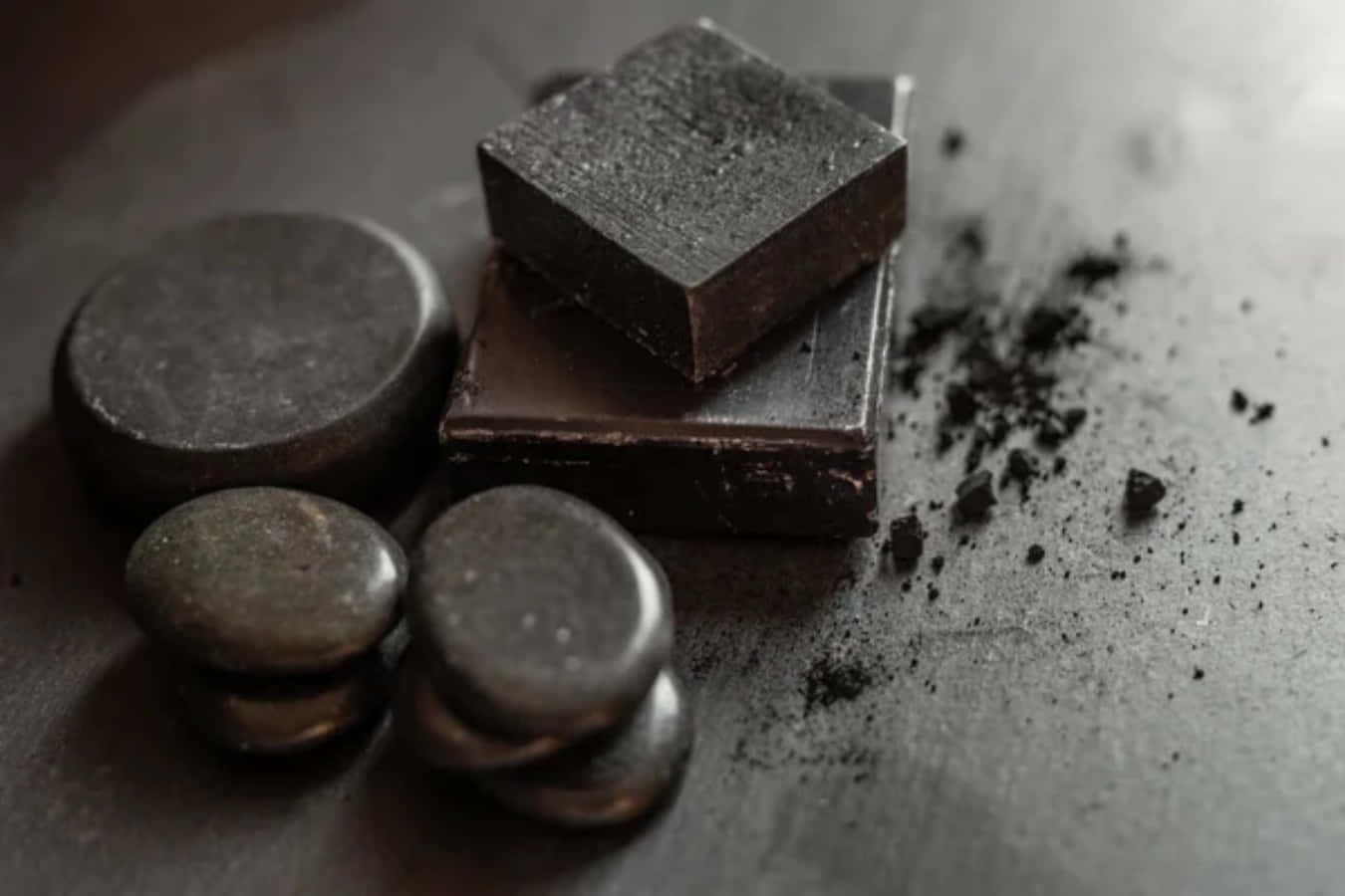 Black Soap 桌布 壁紙 — 黑巧克力條和光滑的石頭放在帶有碎屑的紋理灰色表面上。
