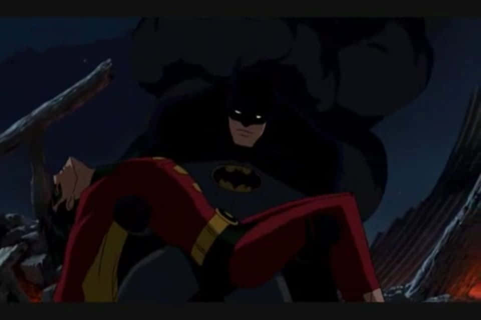 Batman Death In The Family 桌布 壁紙 — 黑暗動畫風格的蝙蝠俠在夜晚城市景觀中抱著一個身穿紅色西裝的人物，背景有火焰光芒。