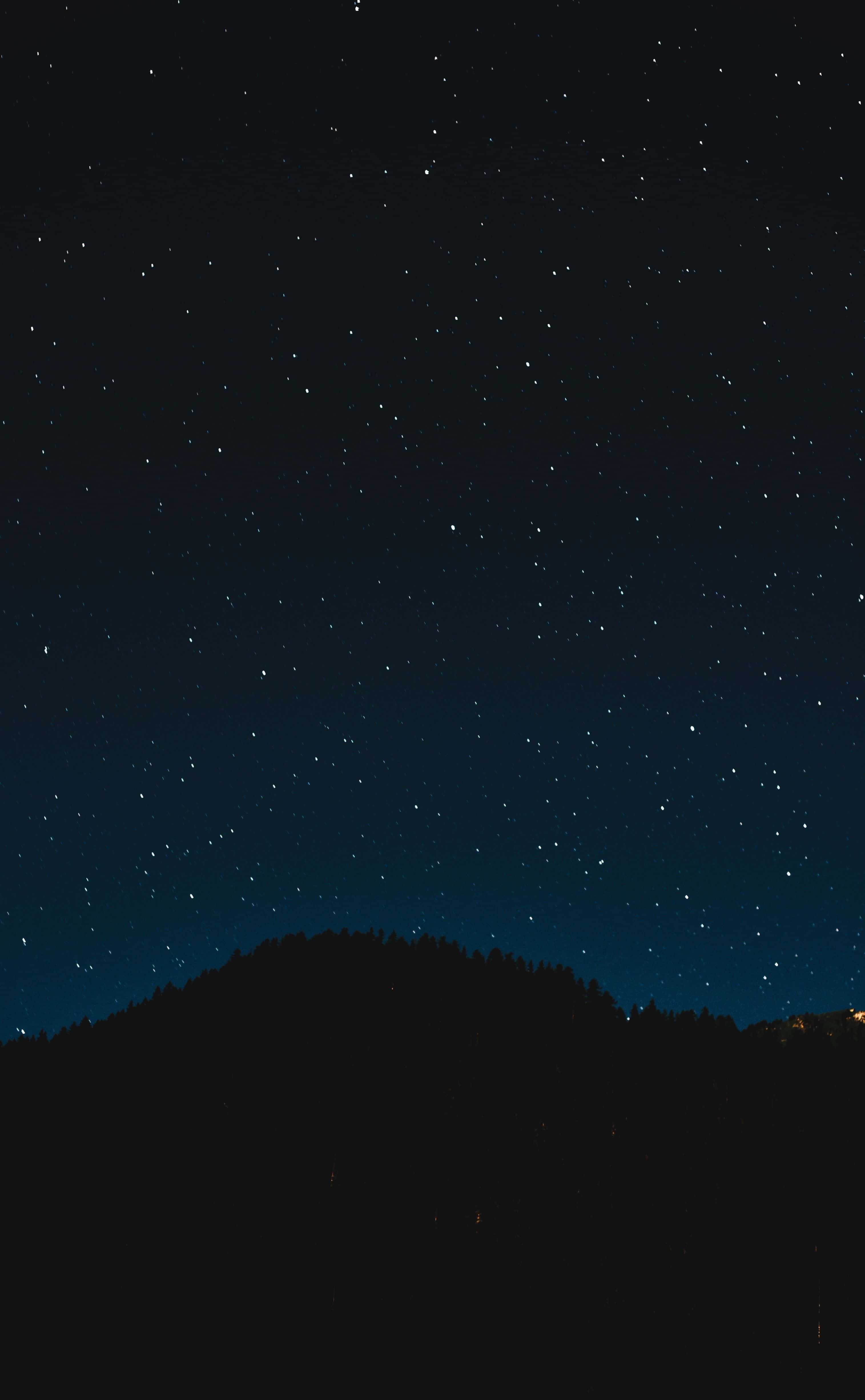 Aesthetic Night Sky 桌布 壁紙 — 黑暗森林山丘上方的星空夜空，地平線上有微弱的遠方燈光。