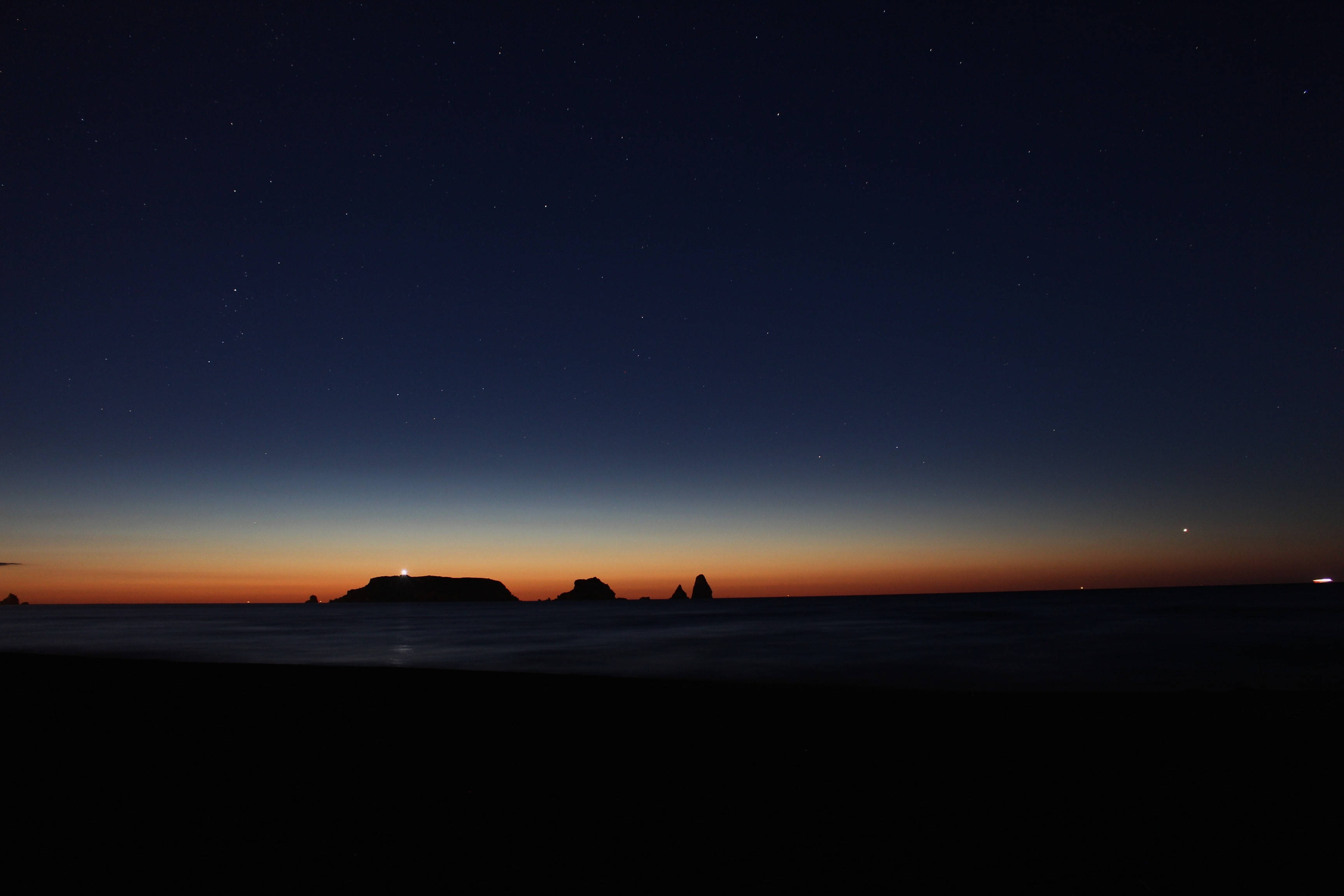 night night 桌布 壁紙 — 黑暗海灘上的星空之夜，剪影岩石形態和發光的地平線。