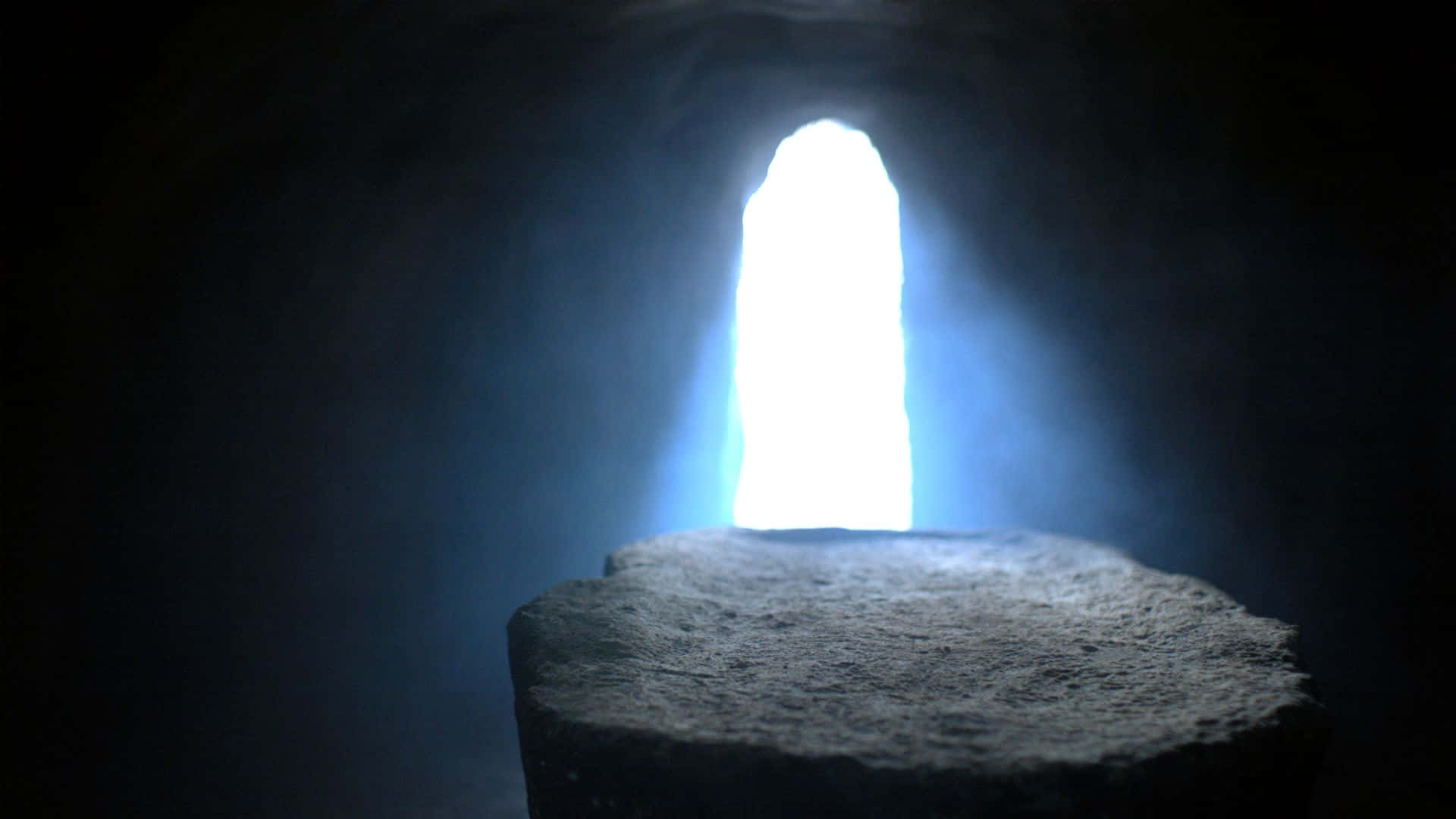 Empty Tomb 桌布 壁紙 — 黑暗隧道中的一個石質基座，被前方拱形開口照射進來的明亮藍光照亮。