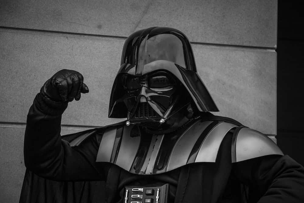 Star Wars Profile 桌布 壁紙 — 黑武士達斯維達身穿標誌性頭盔和盔甲，戴著手套的拳頭舉起靠著素牆的黑白肖像。