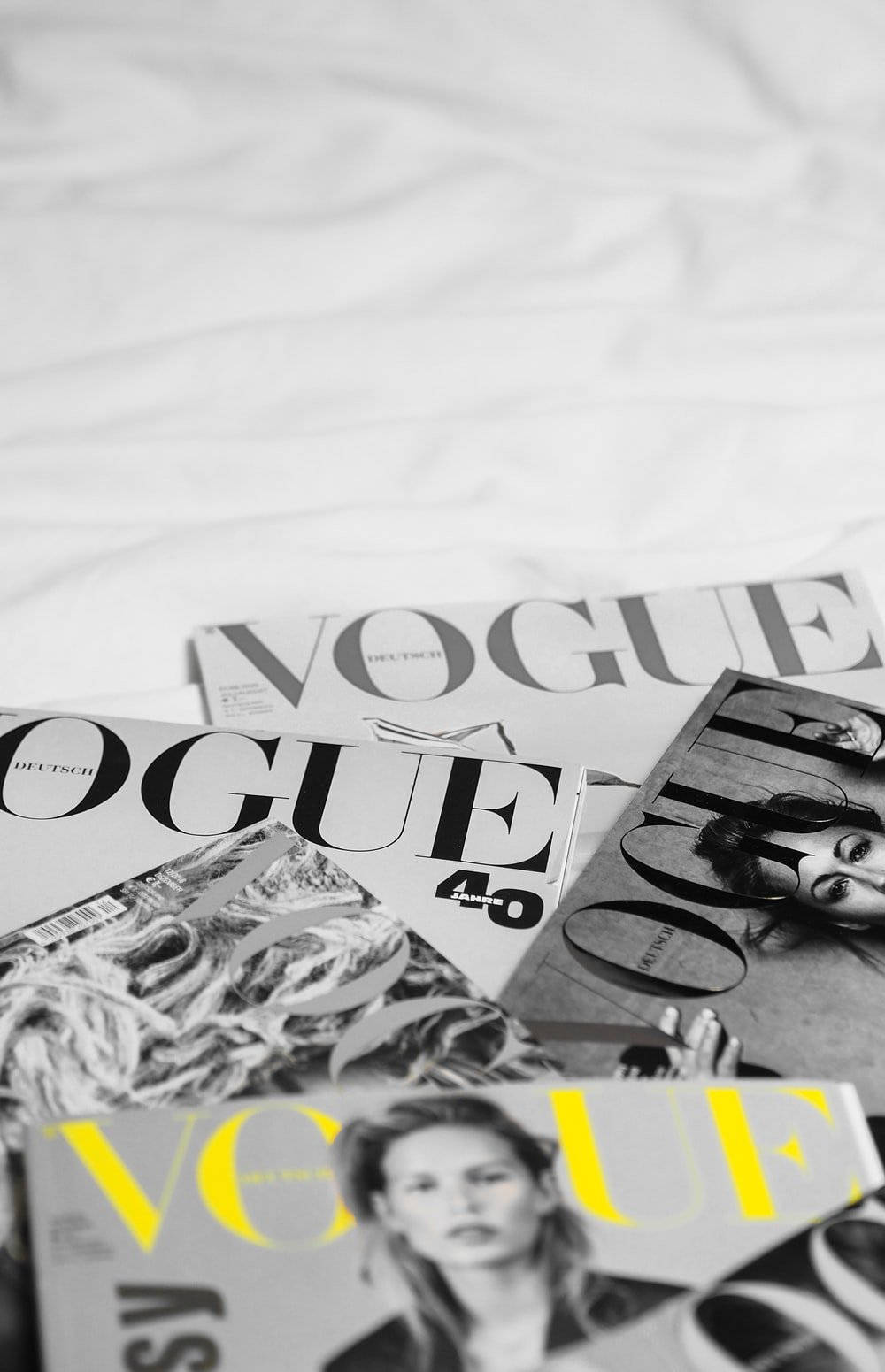 雜誌 桌布 壁紙 — 黑白Vogue雜誌疊在一起，其中一本黃色封面，放在皺巴巴的白色床單上。