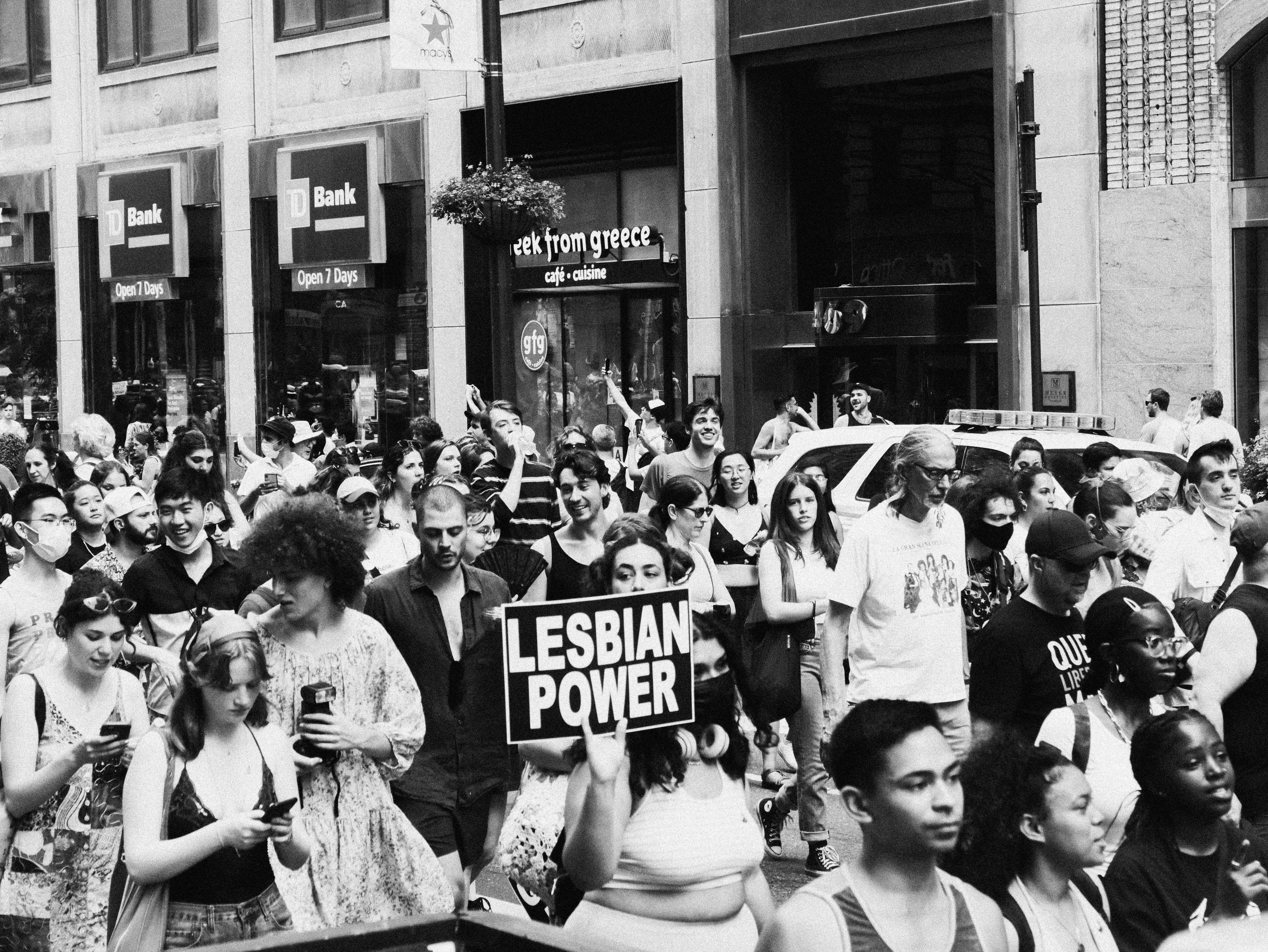 女同志 桌布 壁紙 — 黑白人群在銀行和咖啡店門前舉著「LESBIAN POWER」標語沿著城市街道遊行。