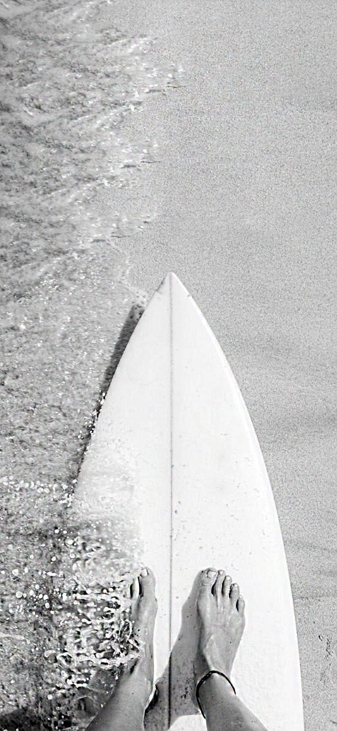 surfing 桌布 壁紙 — 黑白俯視圖，顯示赤腳站在衝浪板上，位於海浪輕拍岸邊的海洋邊緣。