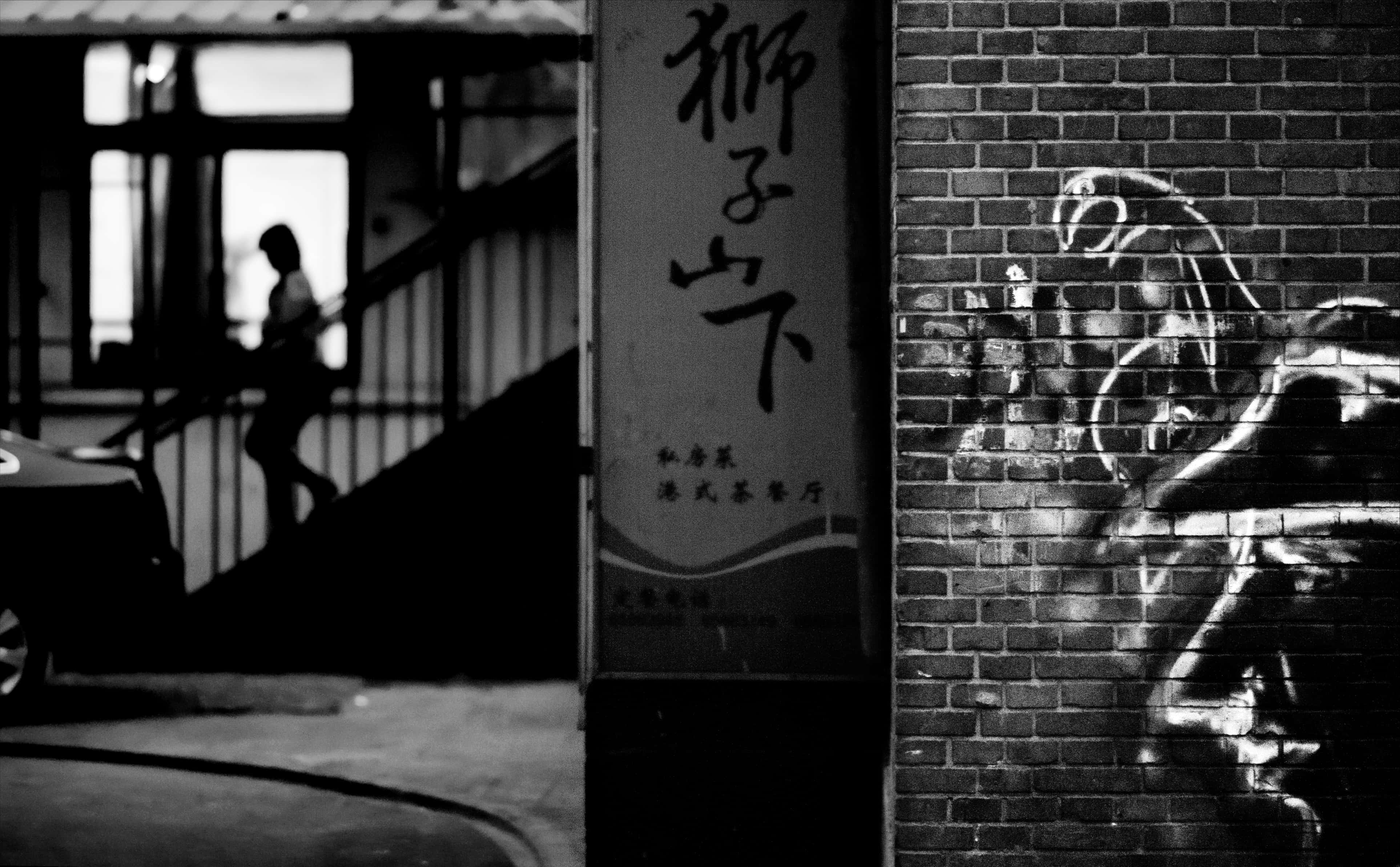 桌布 壁紙 — 黑白城市場景，一個剪影人物在塗鴉和中文標誌的磚牆旁邊上樓梯。