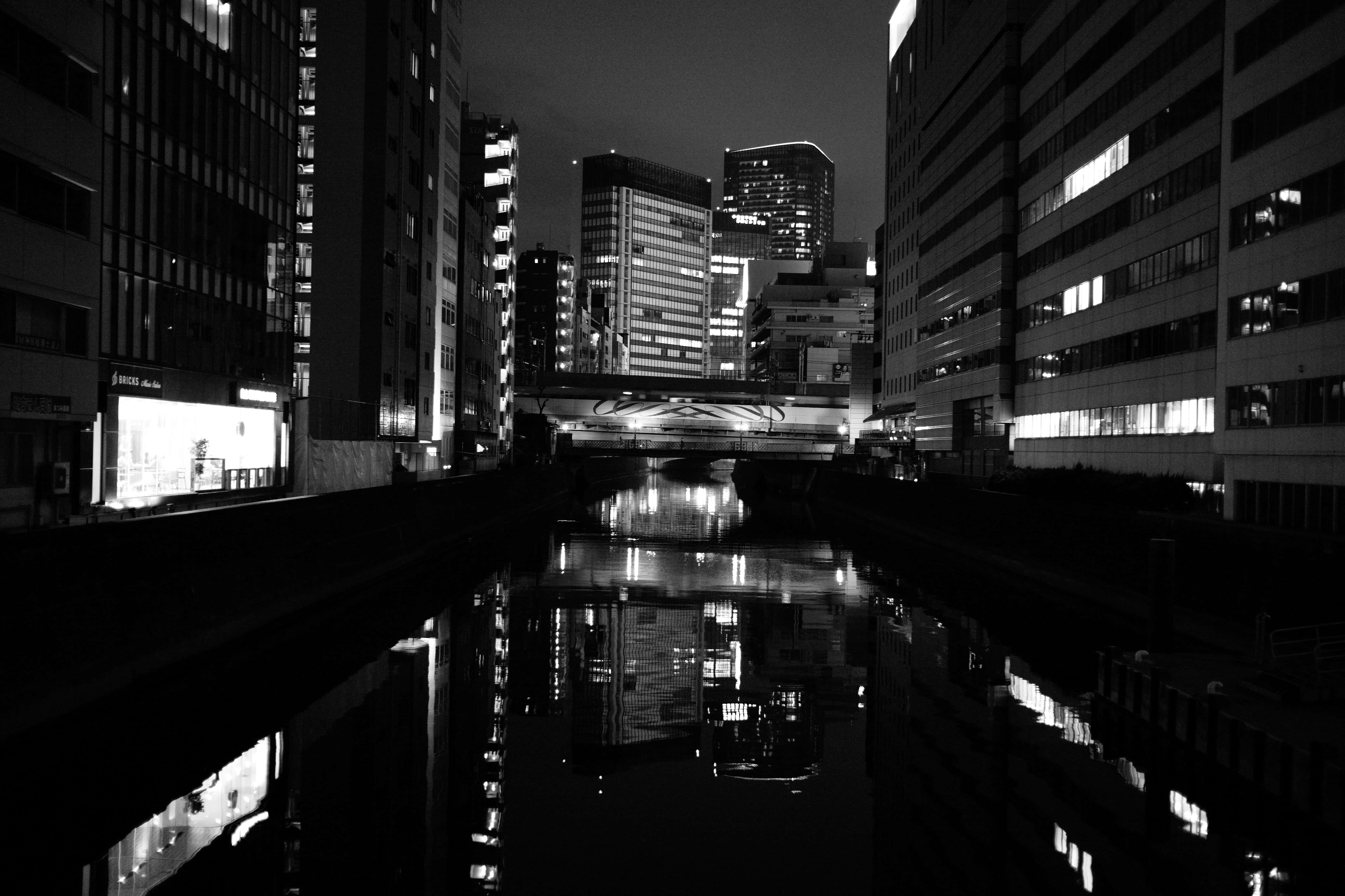 日本 桌布 壁紙 — 黑白城市夜景，顯示運河倒映著燈火通明的摩天大樓以及高聳建築之間的橋樑。