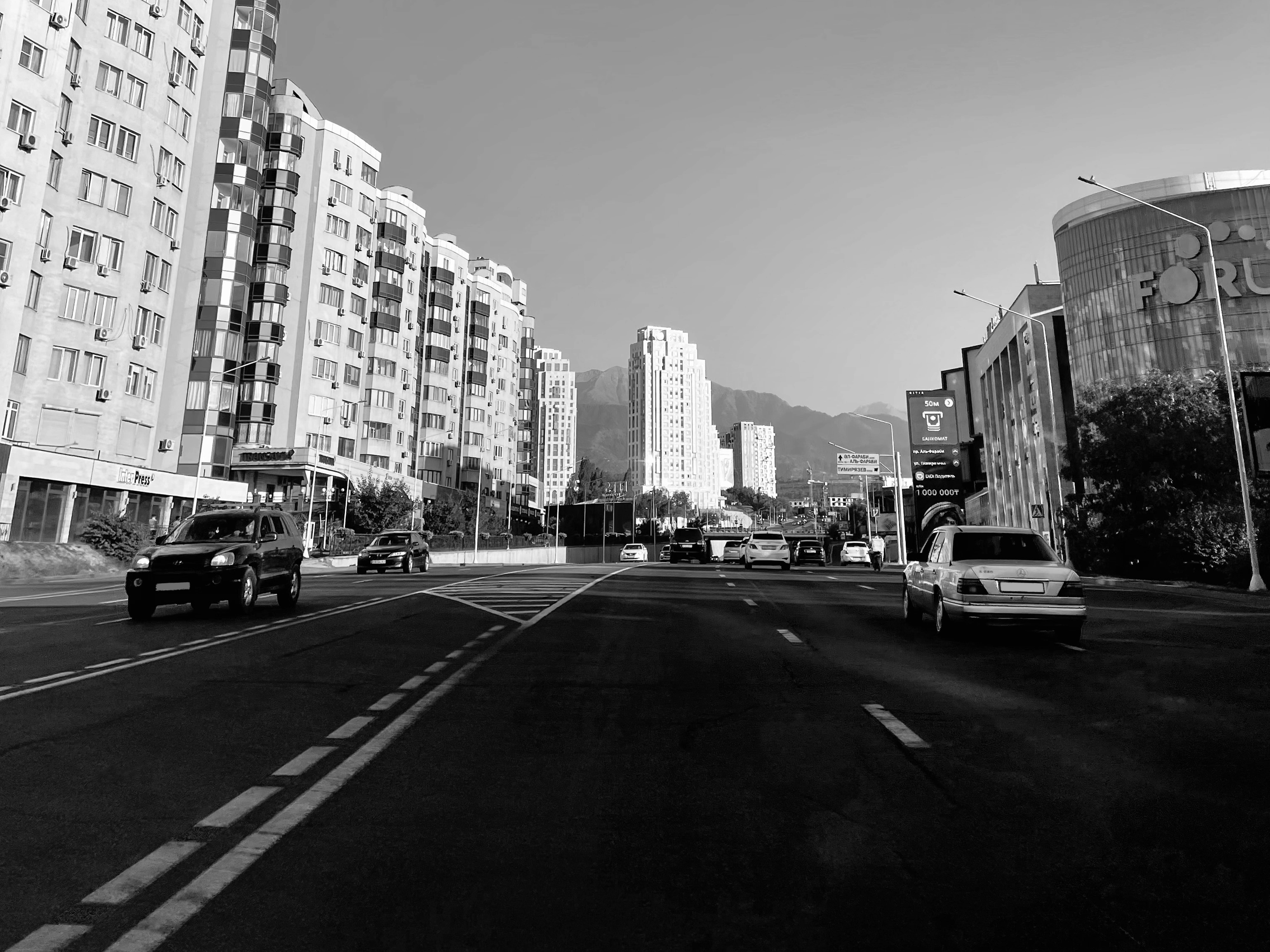 Kazakhstan 桌布 壁紙 — 黑白城市街景，汽車駛過高樓大廈和遠山，天空晴朗。