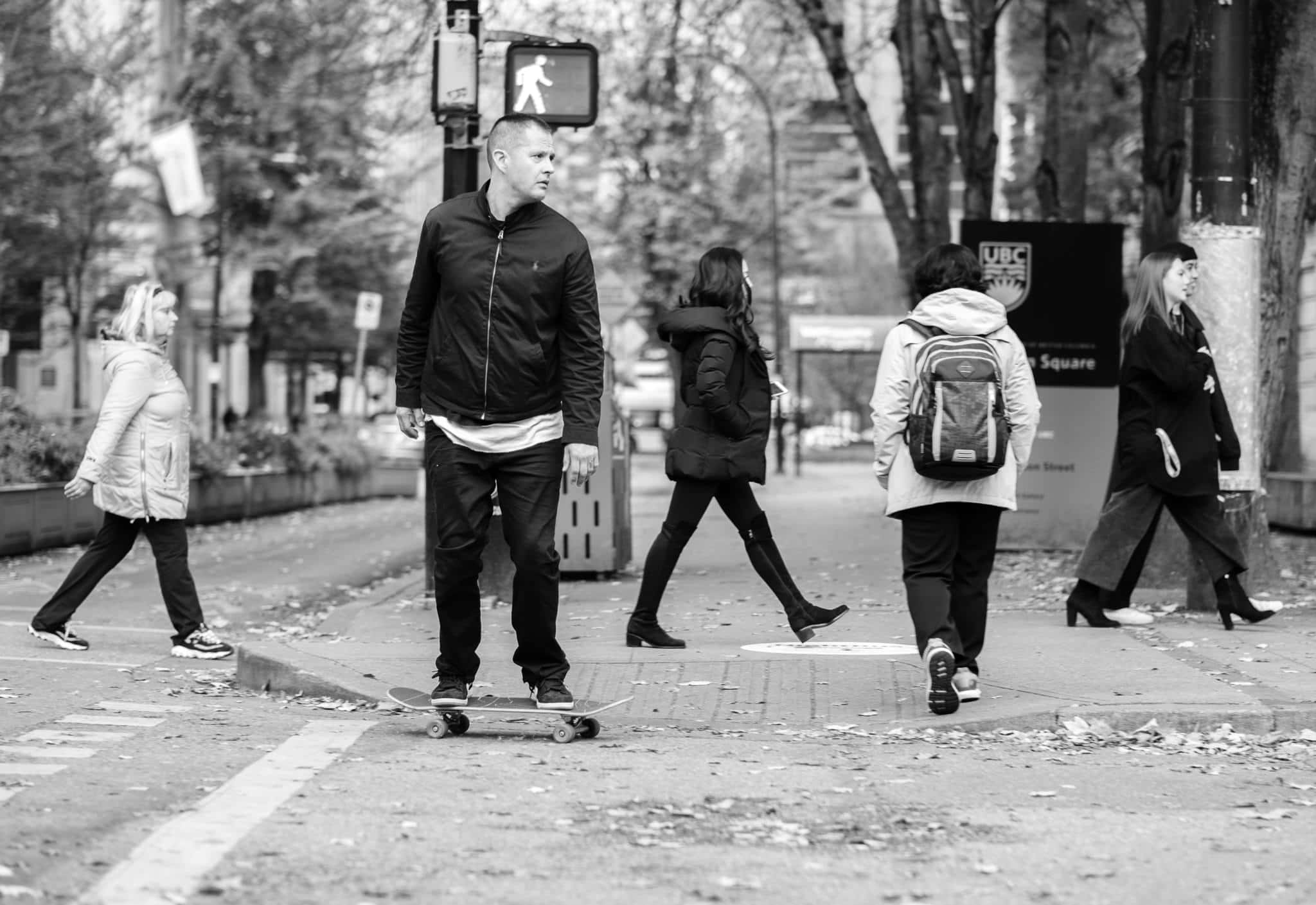 滑板 桌布 壁紙 — 黑白城市街景，行人過馬路，一名男子踩滑板在落葉中。