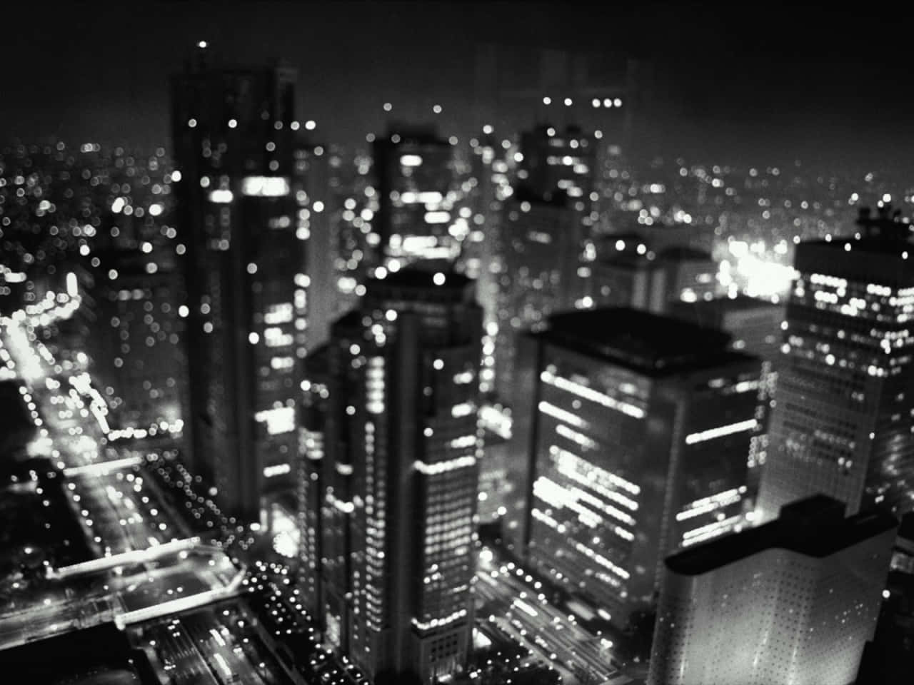 Beautiful Black And White 桌布 壁紙 — 黑白夜景城市景觀，模糊的摩天大樓和發光的燈光營造出夢幻般的城市光芒。