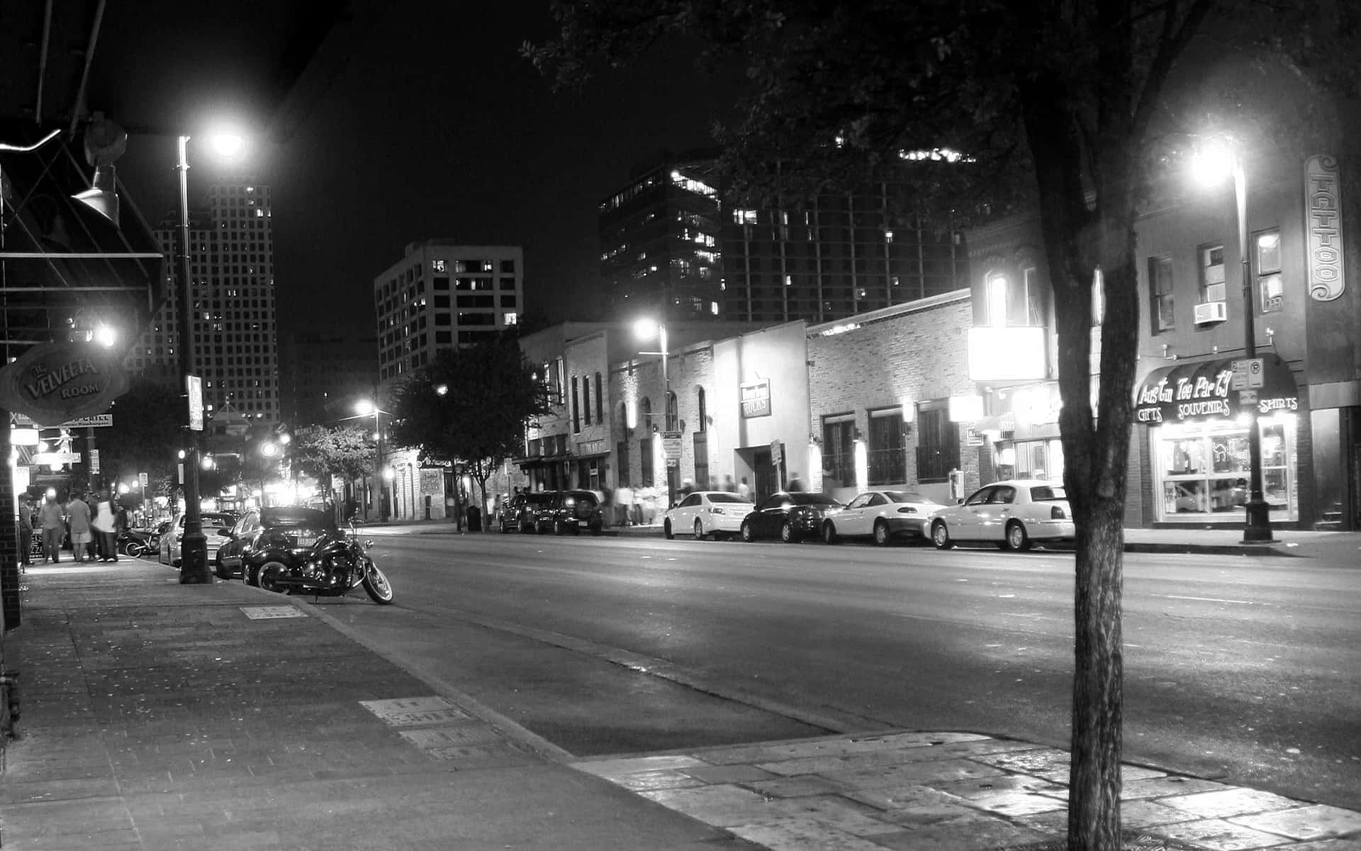 Night Street 桌布 壁紙 — 黑白夜景城市街道場景，有停泊的汽車、發光的街燈和行人道上的行人。
