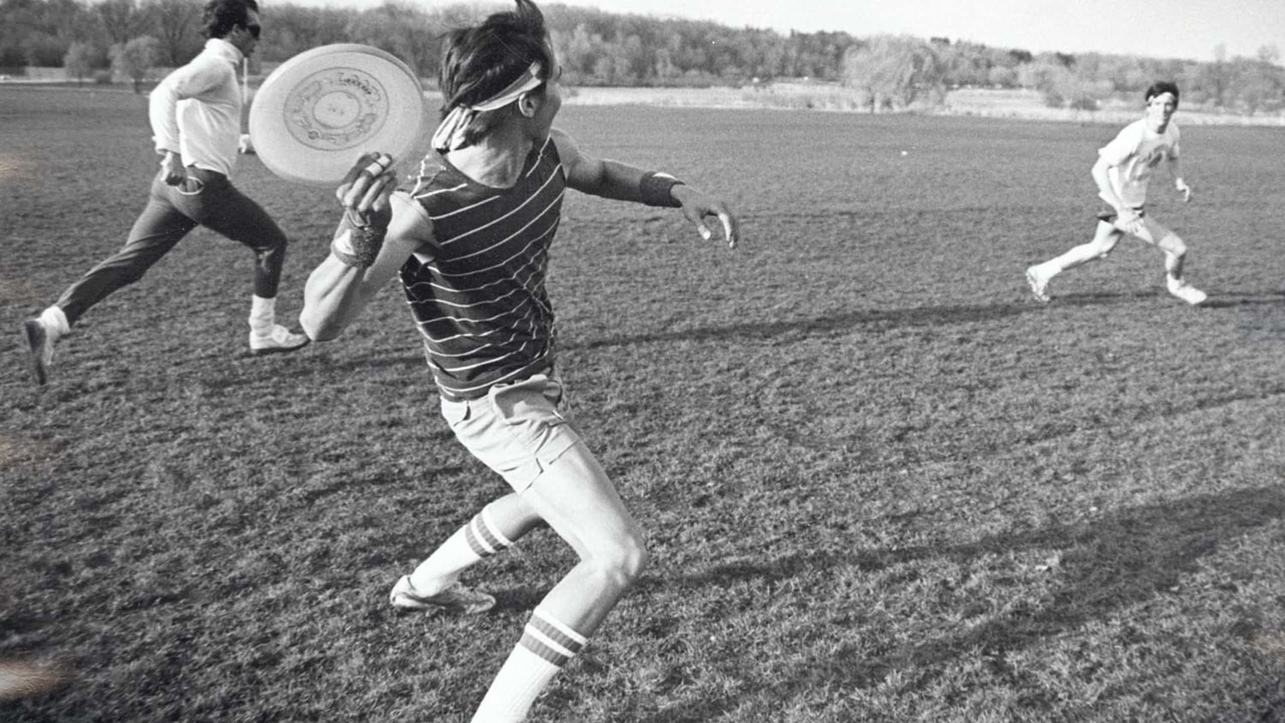 1440p Ultimate Frisbee 桌布 壁紙 — 黑白照片，三人在草地上玩飛盤，背景有樹木。