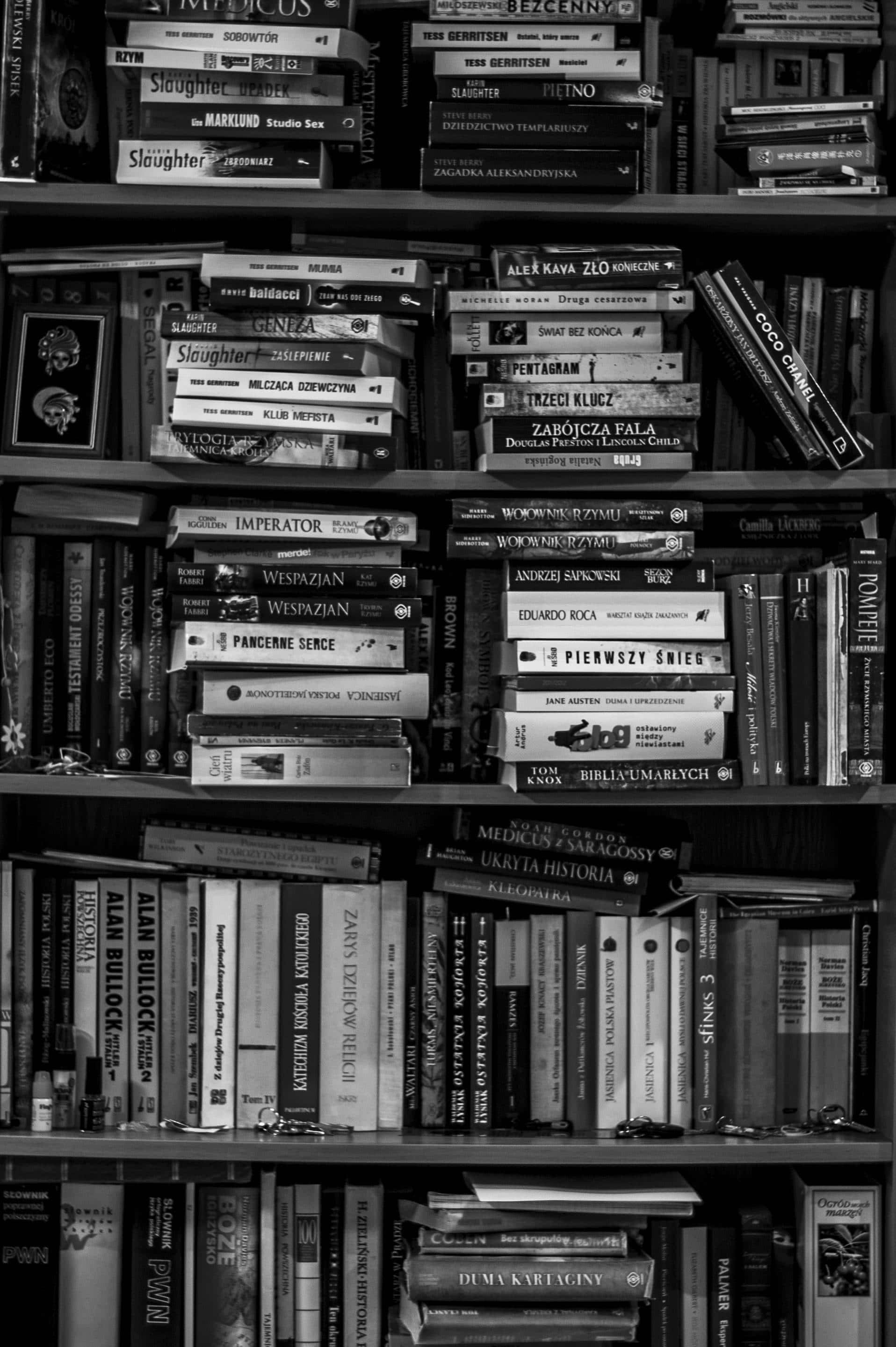 Dark Book Aesthetic 桌布 壁紙 — 黑白照片，展示密集的書架上擺滿了各種字體和方向的波蘭語書籍。
