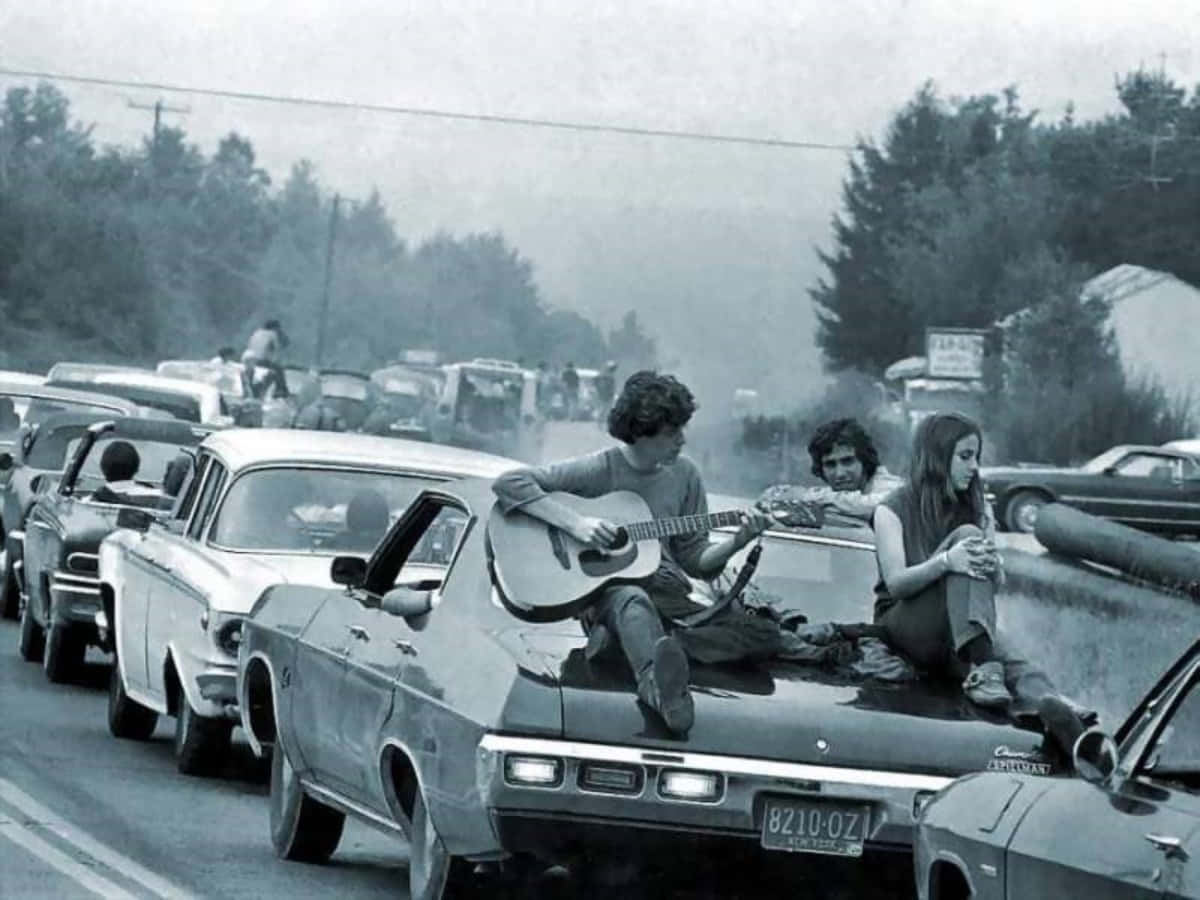 woodstock 桌布 壁紙 — 黑白照片，年輕人在交通堵塞中坐在車頂上彈吉他和放鬆。