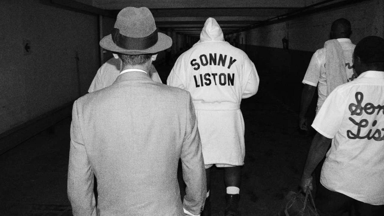 Boxing 桌布 壁紙 — 黑白照片，男人們沿著昏暗的走廊走開，其中一人穿著「SONNY LISTON」長袍。