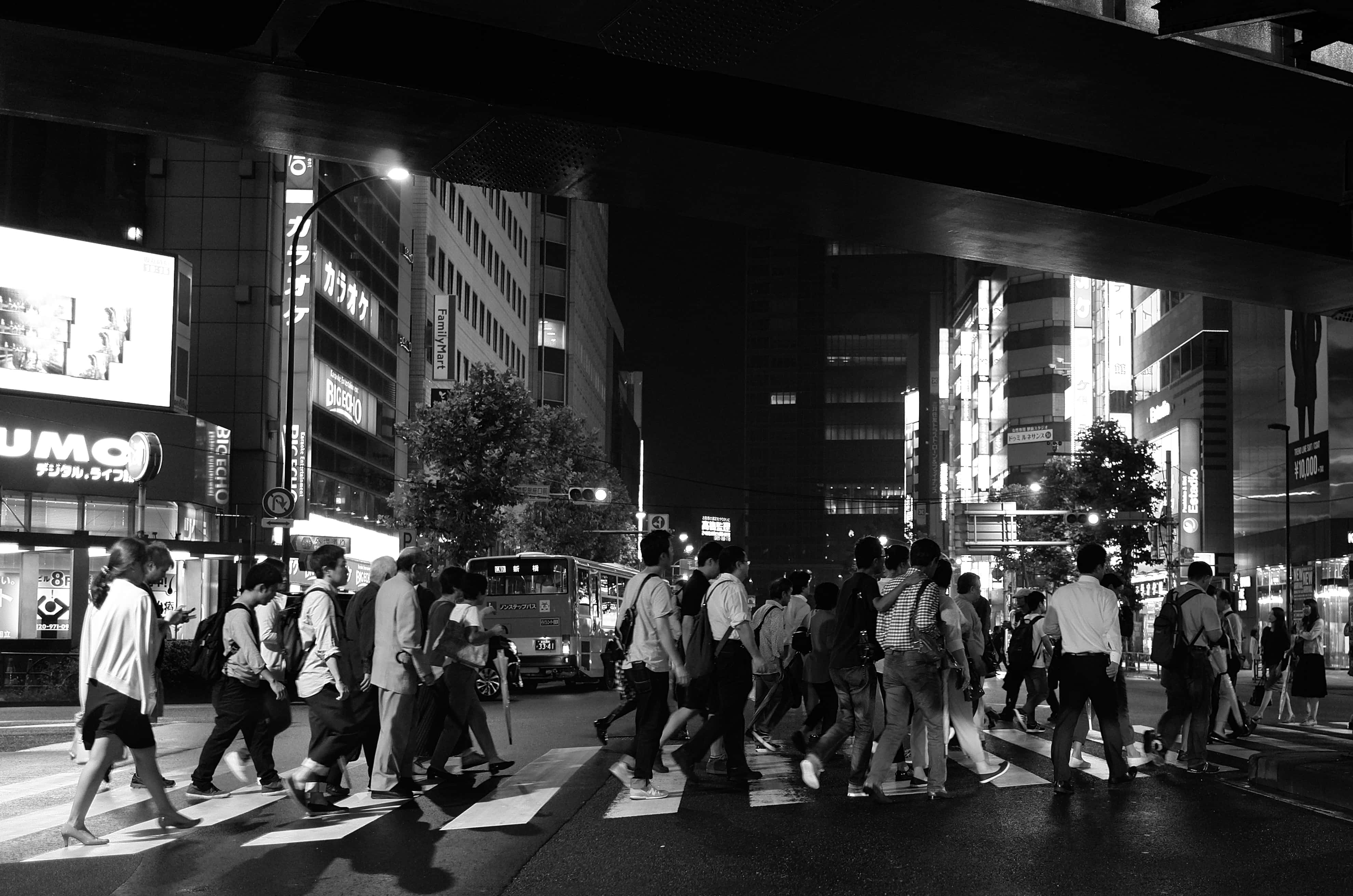 日本黑白 桌布 壁紙 — 黑白照片，行人在夜晚於發光的霓虹招牌和高聳建築物下穿越繁忙的東京街道。