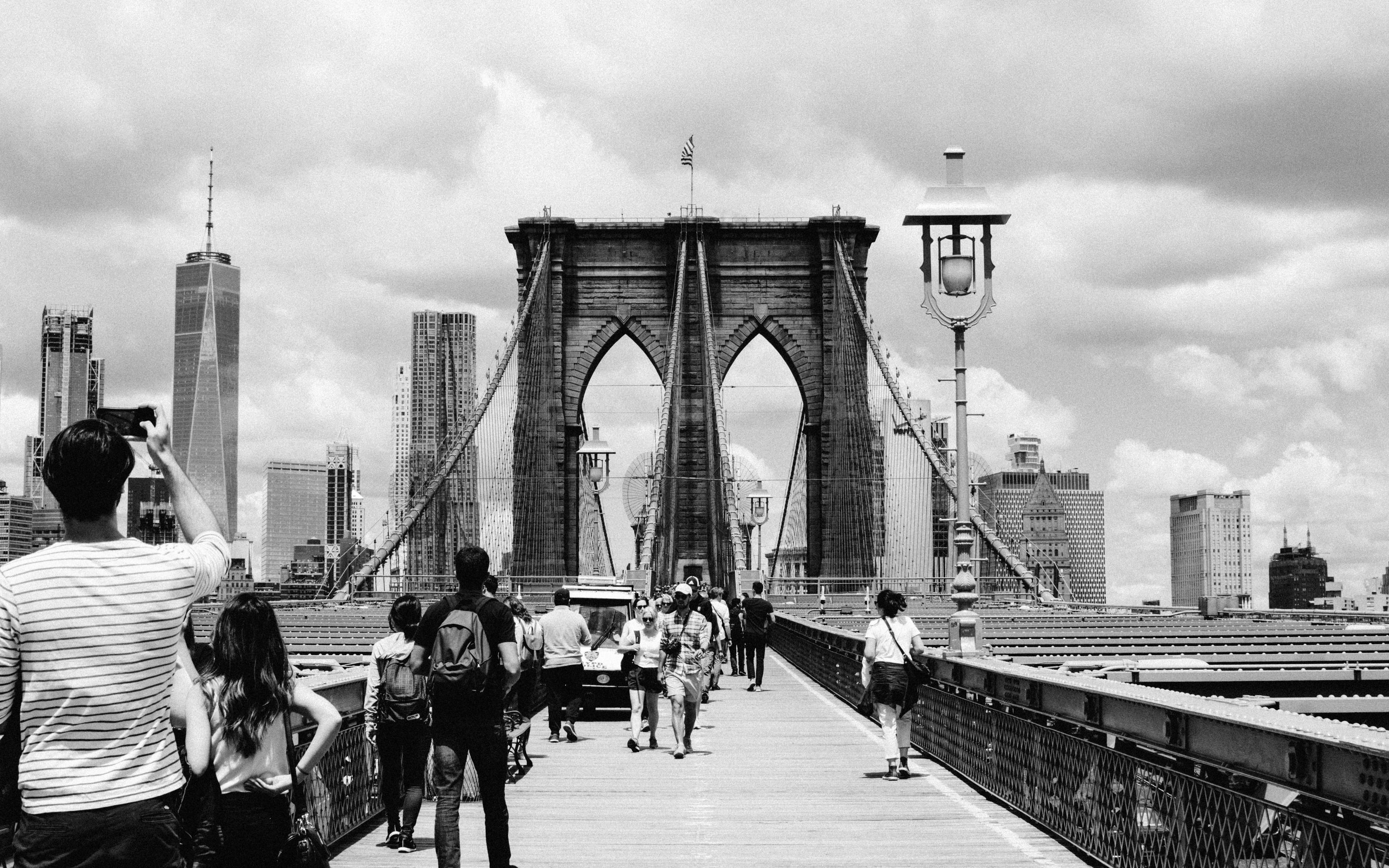 Brooklyn Bridge 桌布 壁紙 — 黑白照片，行人正在布魯克林大橋上行走，背景是紐約市天際線，天空多雲。