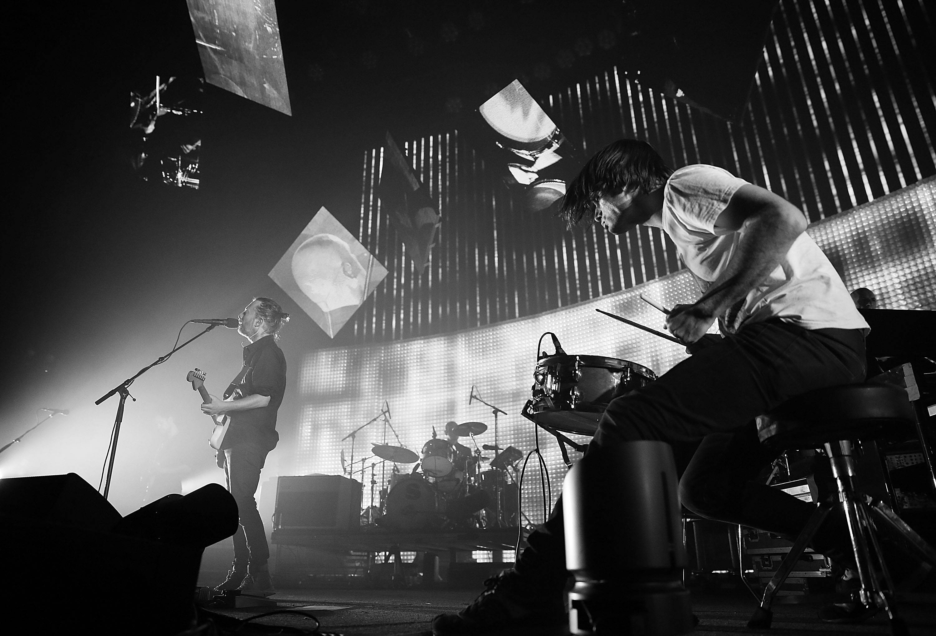 band 桌布 壁紙 — 黑白照片，音樂家在舞台上現場表演，帶有戲劇性燈光和懸掛螢幕。
