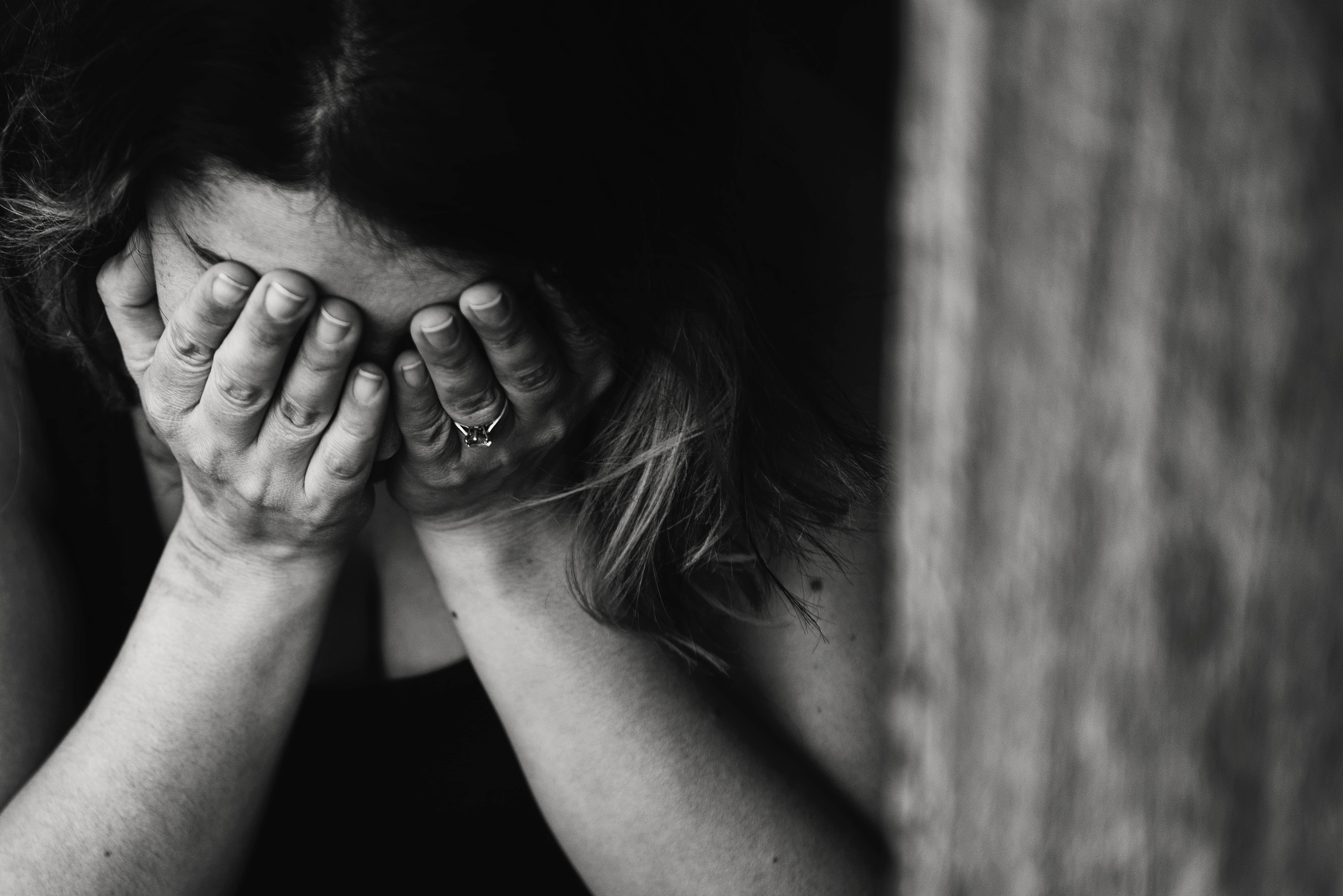 anxious 桌布 壁紙 — 黑白照片中，一個人在木質表面附近用手遮住臉，傳達深深的痛苦。