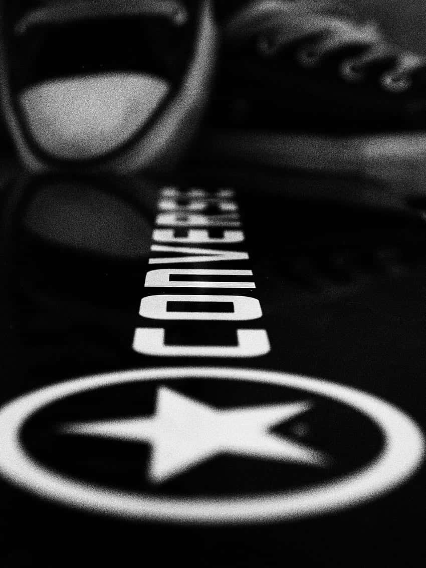 Converse 桌布 壁紙 — 黑白特寫，Converse 運動鞋標誌投射在反光表面上，背景有模糊的鞋子。