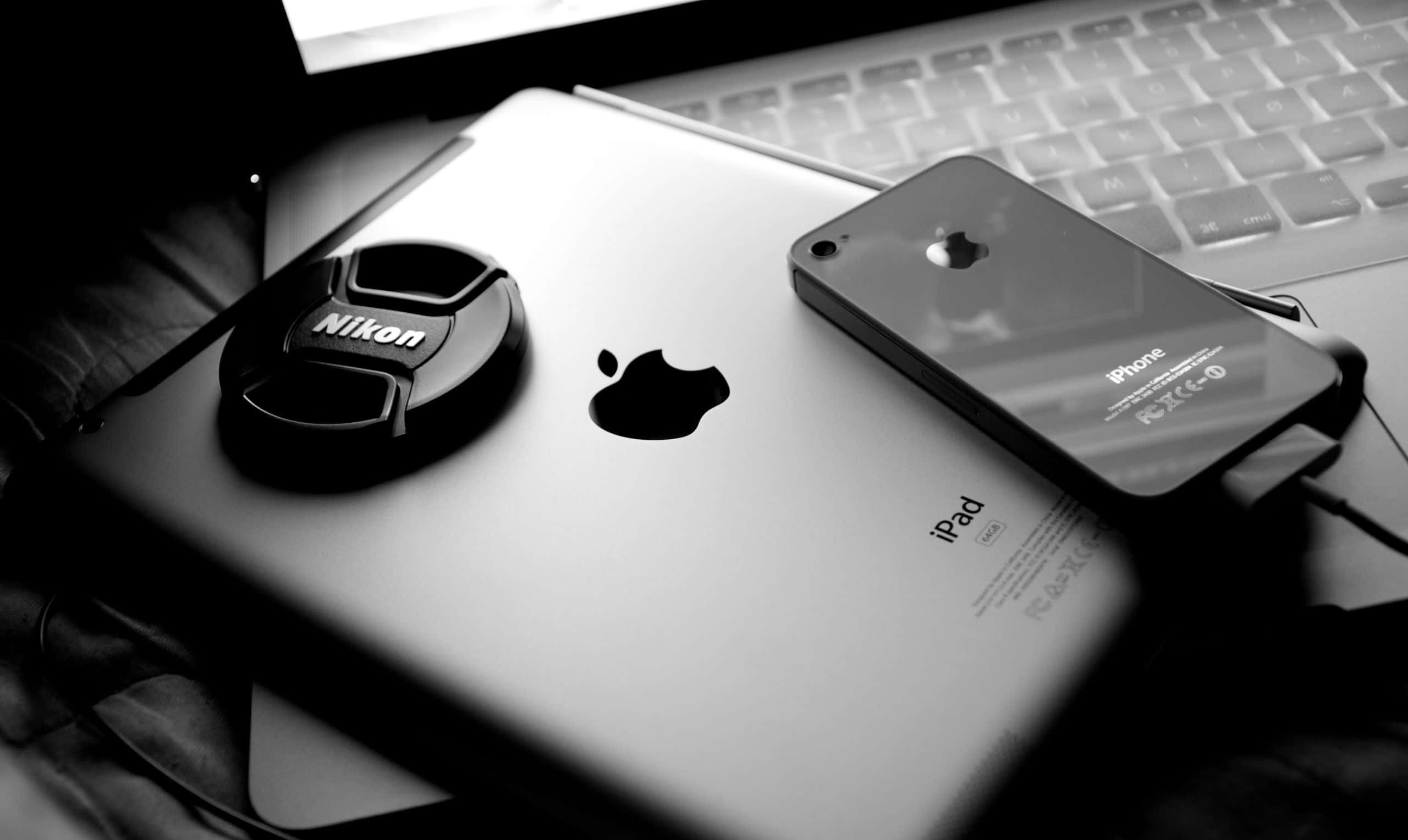 攝影 桌布 壁紙 — 黑白特寫，Nikon鏡頭蓋放在iPad上，旁邊有iPhone和筆記型電腦鍵盤。