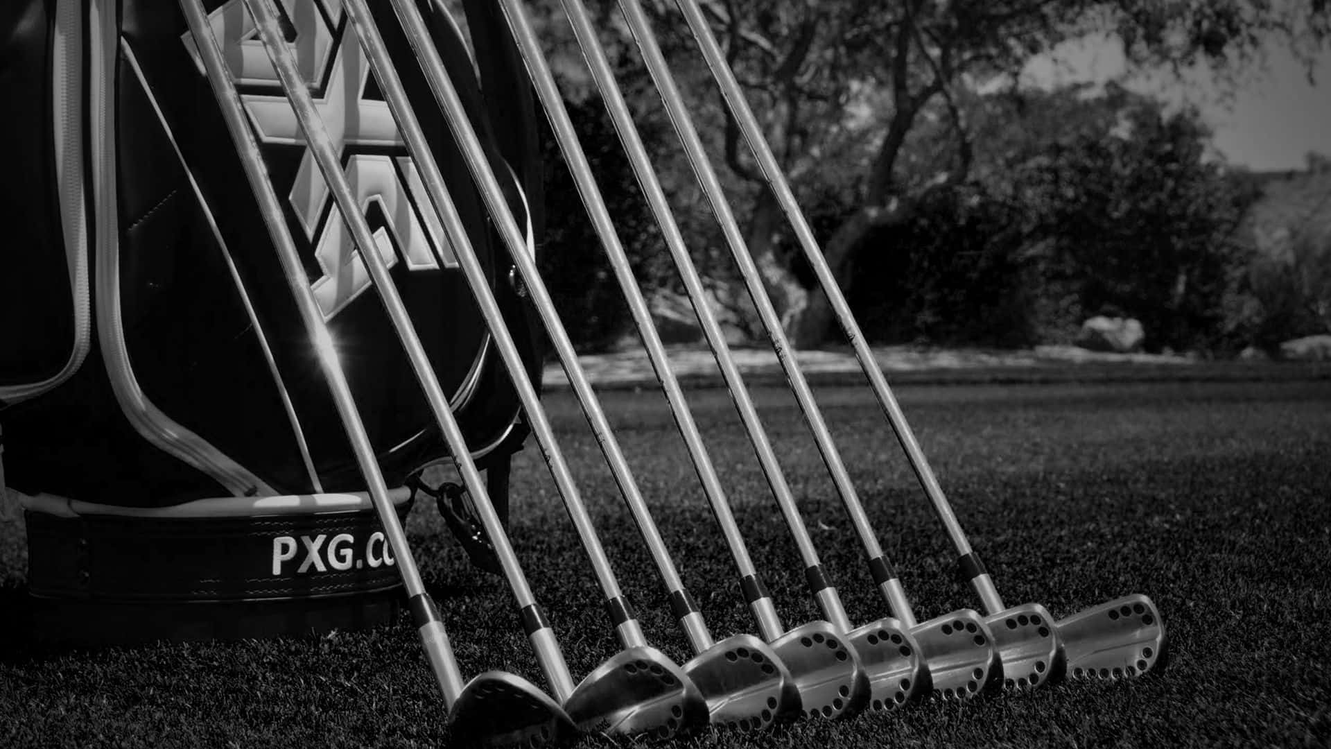 Golf Club 桌布 壁紙 — 黑白特寫，PXG高爾夫球桿在草地上扇形展開，旁邊有一個品牌球袋，背景樹木柔焦。
